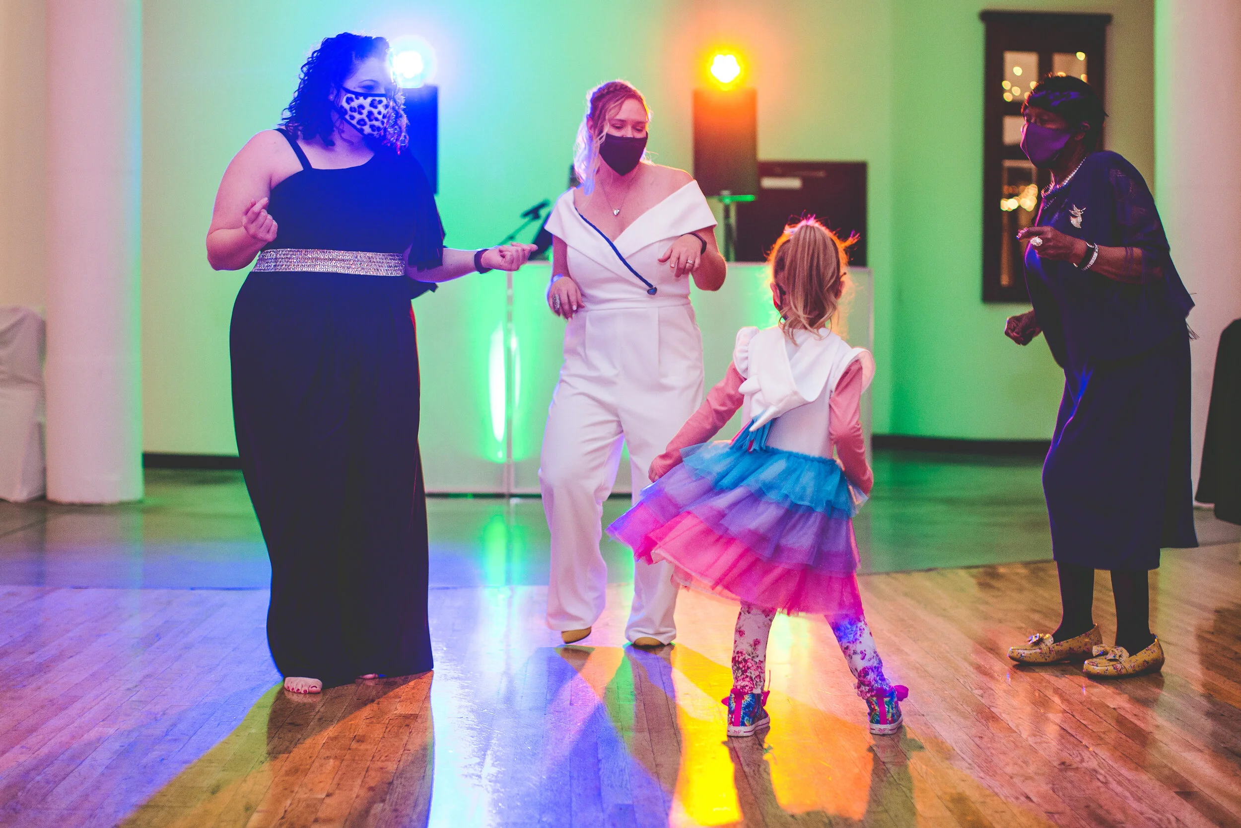 Guests and a bride masked up for Covid dance around the flower girl during a wedding reception.