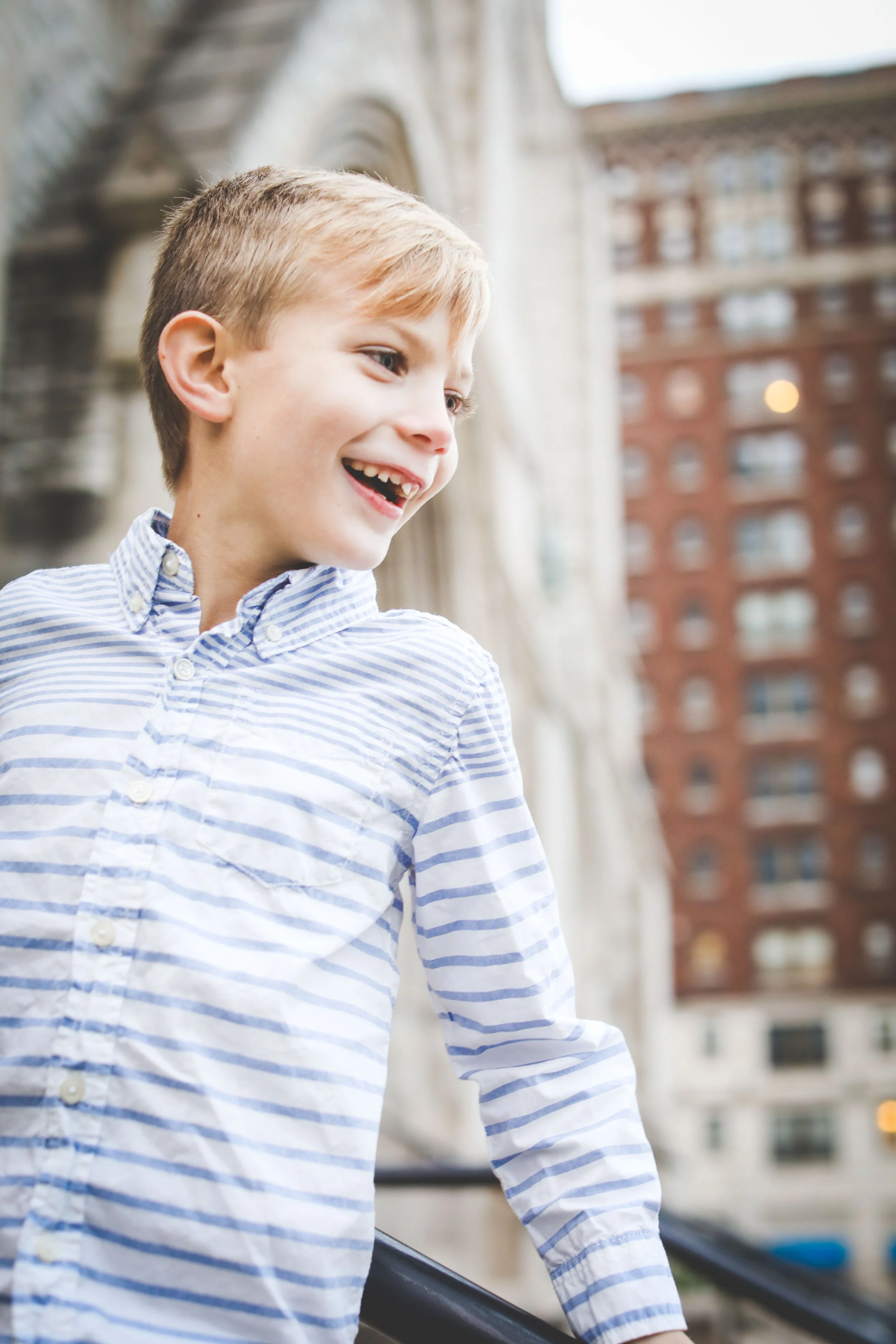 Portrait of a boy looking off-camera and smiling in front of tall urban buildings.