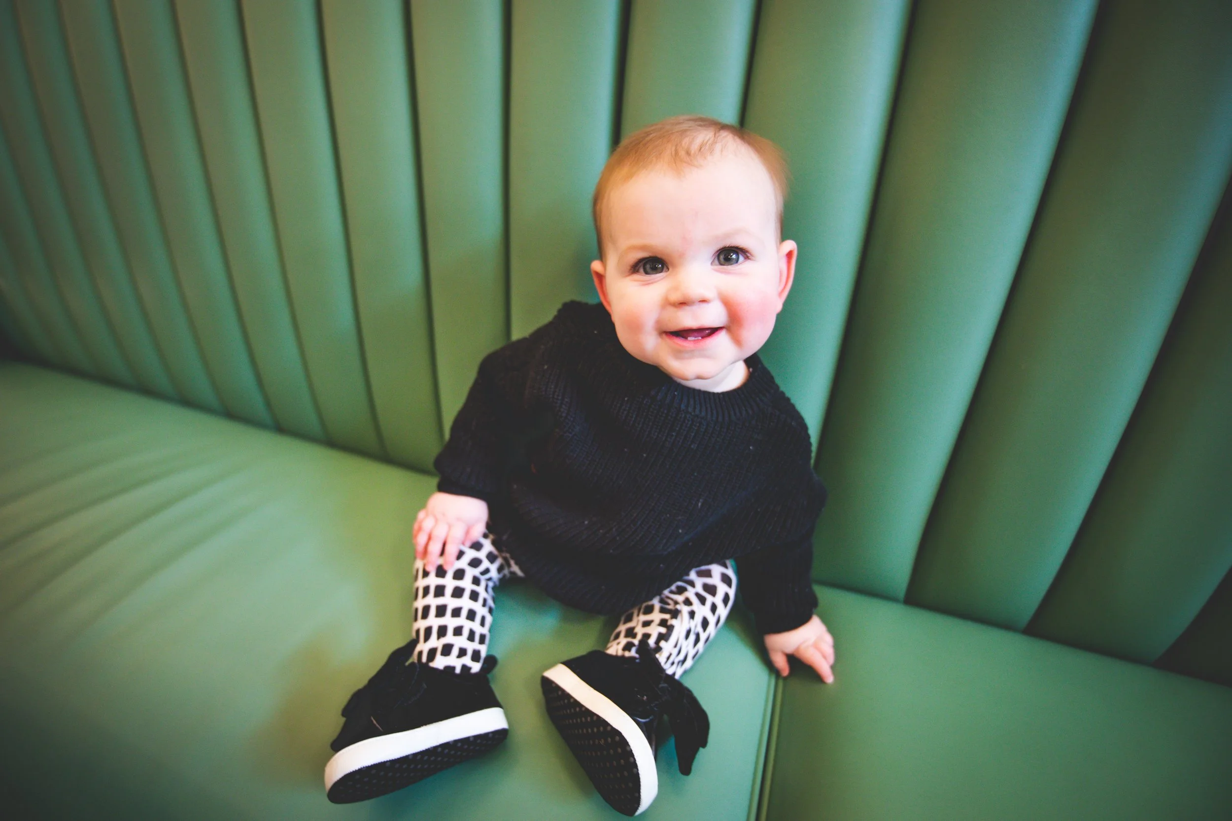 First birthday photo shoot of a baby girl dressed in black and white sitting on the green retro bench at the Soda Fountain in Saint Louis.