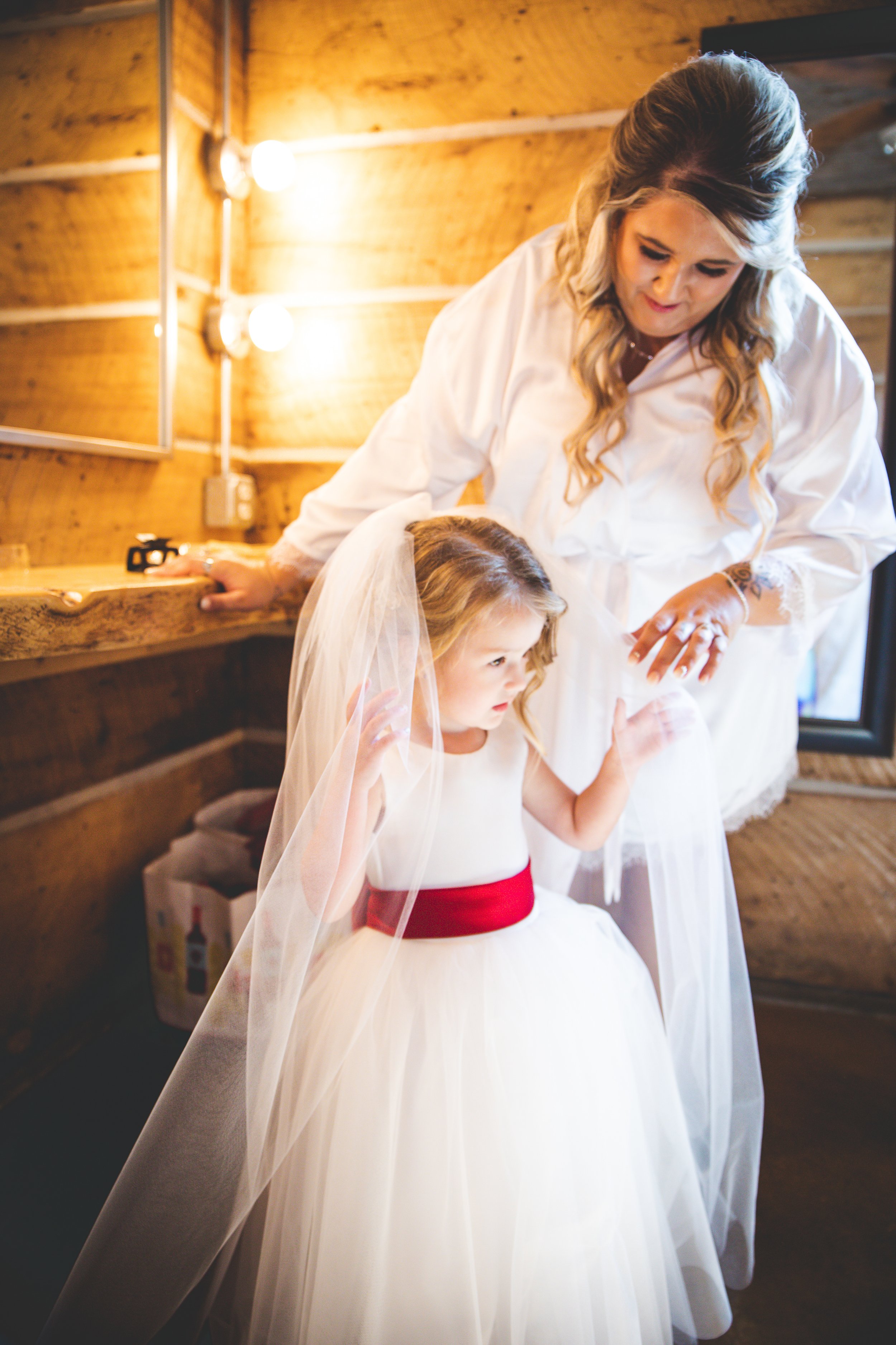 A sweet getting ready photo of a bride holding her young daughter's hand. The daughter is wearing the bride-to-be's veil. 
