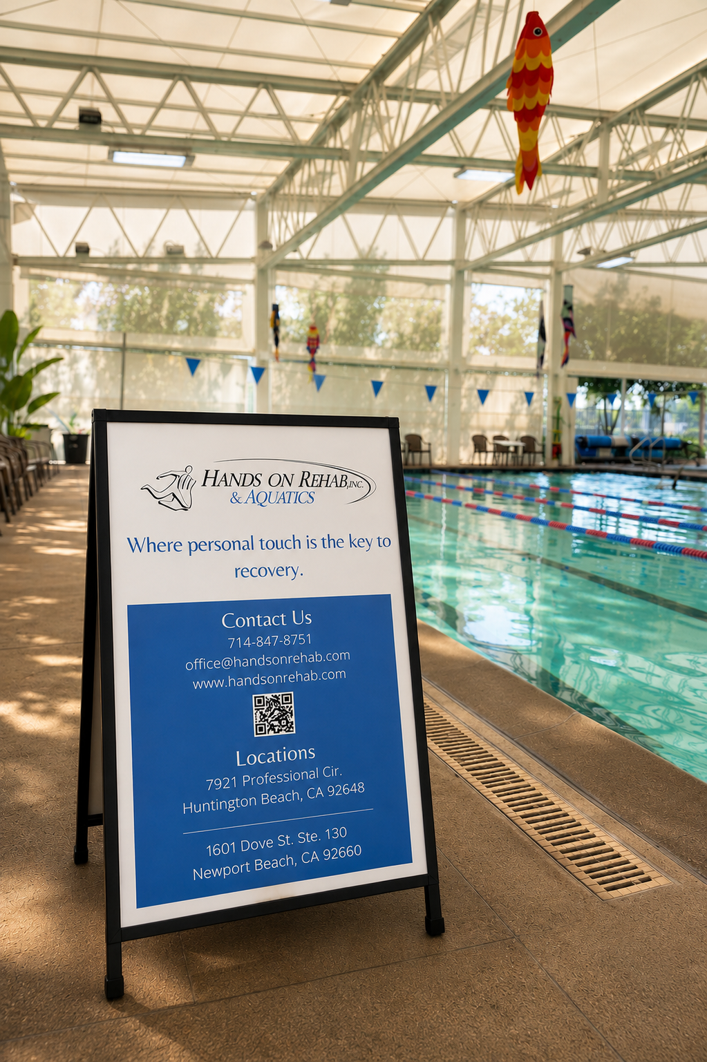An indoor swimming pool with a sign advertising Hands on Rehab & Aquatics, featuring contact information and locations in Huntington Beach and Newport Beach, California.