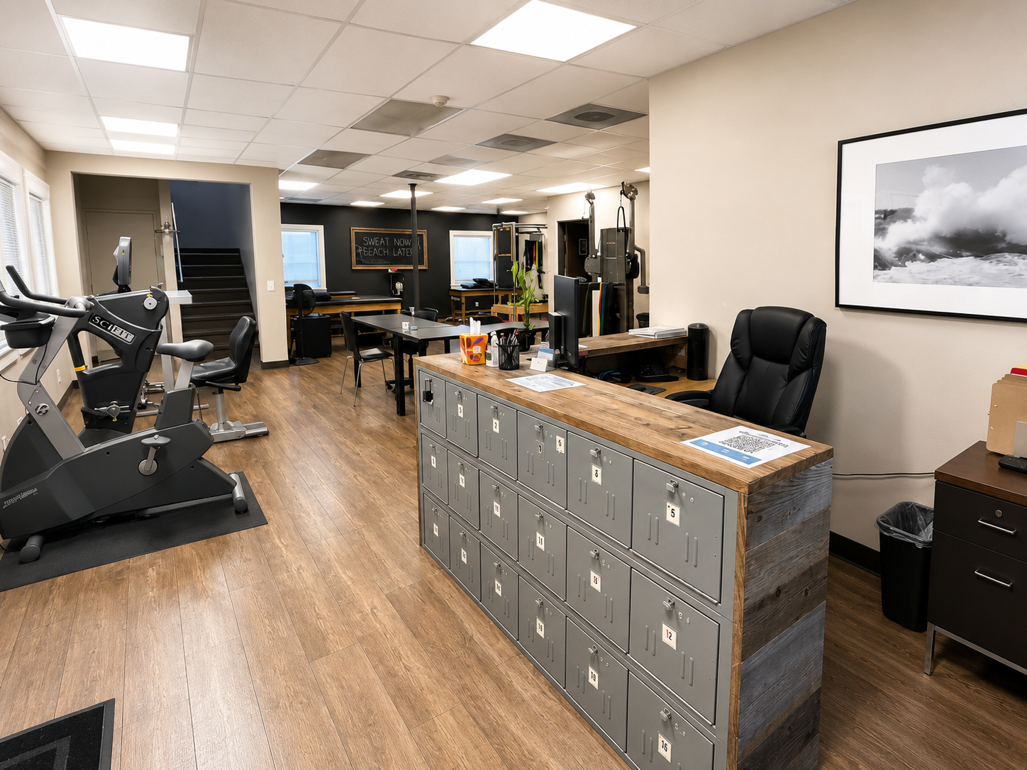 A modern gym and office space with fitness equipment, lockers, desks, and office chairs.