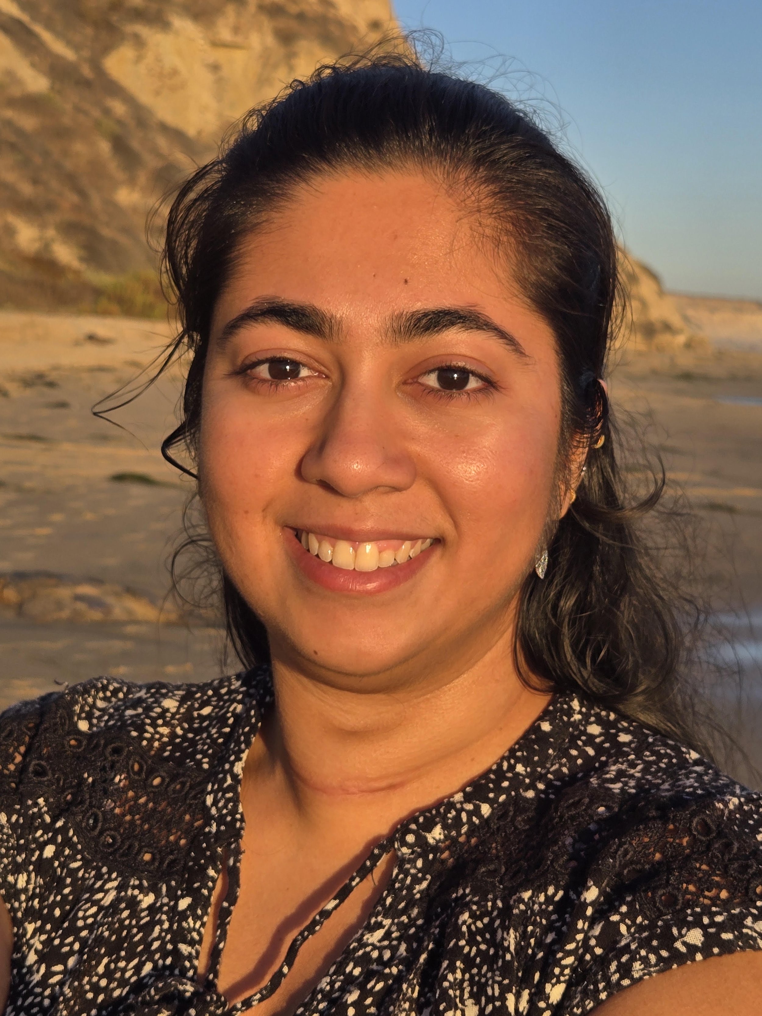 Close-up of a smiling woman outdoors at sunset with mountains in the background.