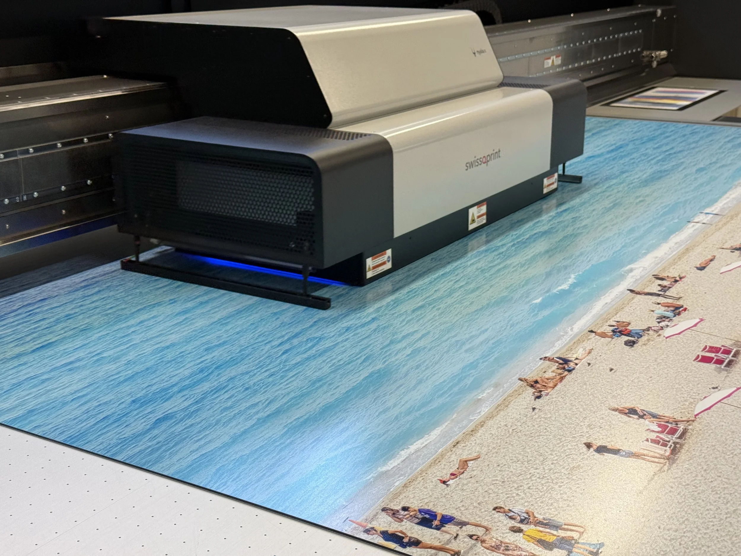 Large format printer printing a beach scene with people on the sand and ocean nearby.