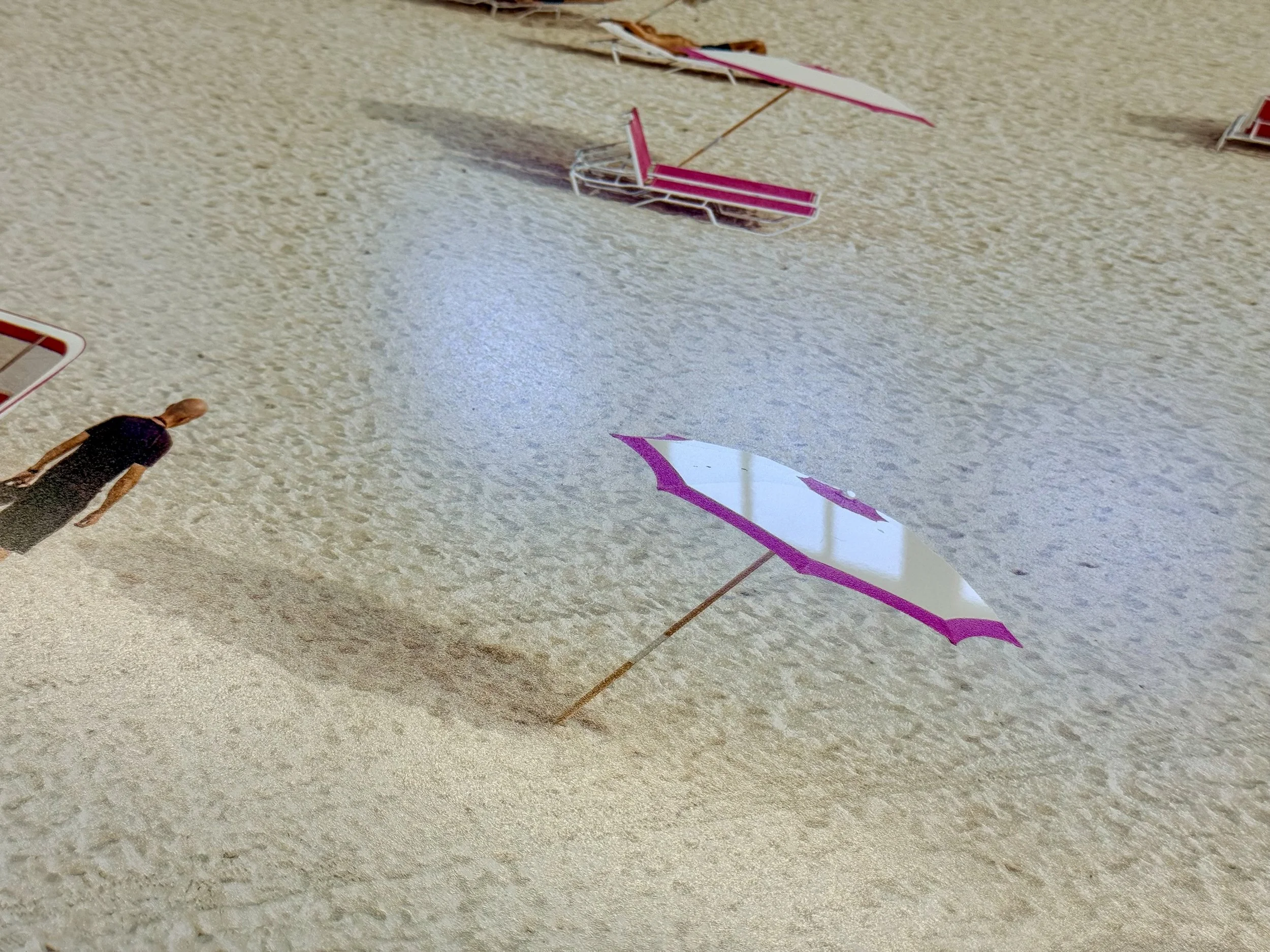 Colorful paper and stick kite flying on a beige carpeted floor with a person standing nearby.