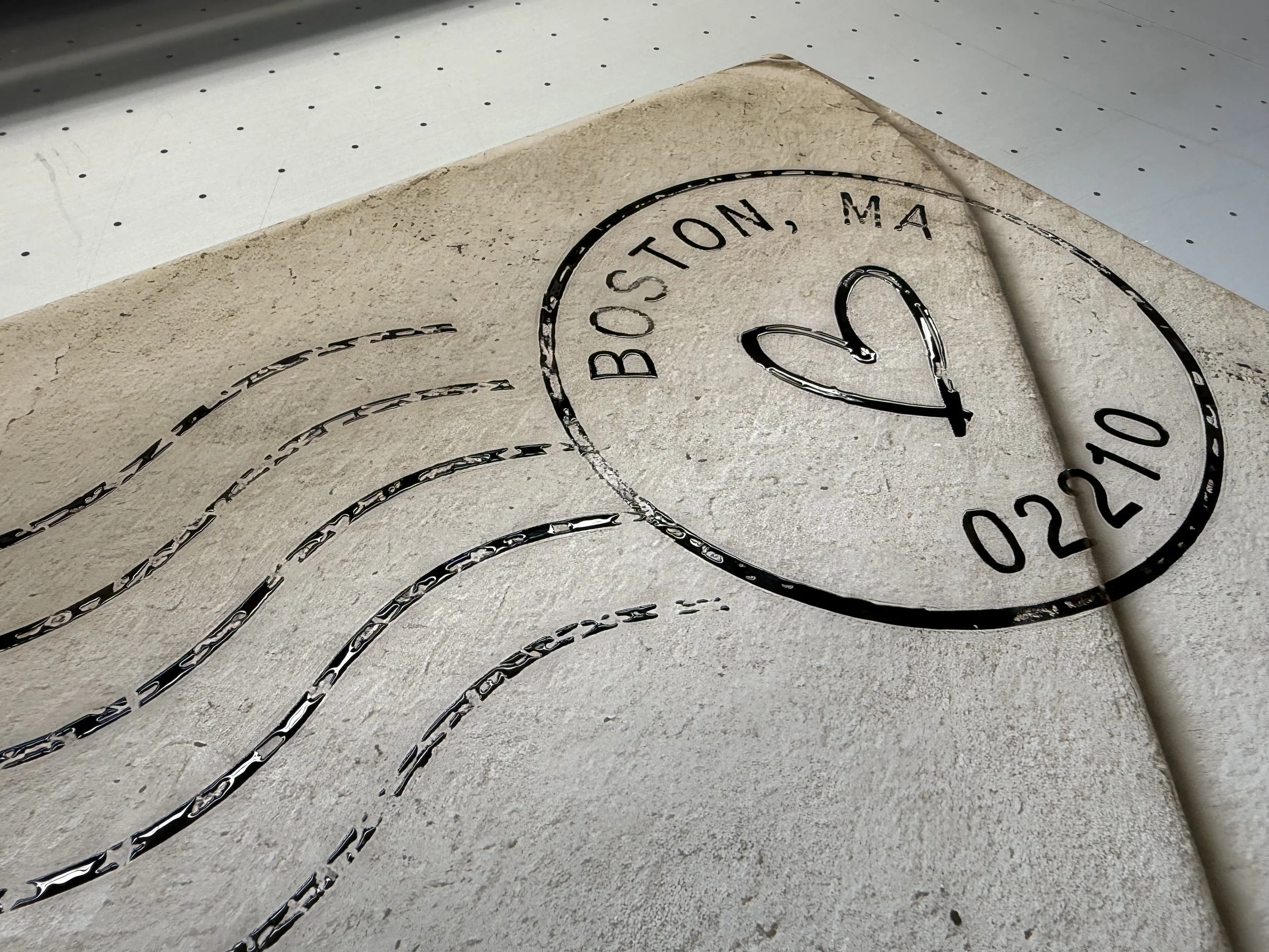Close-up of a textured surface with black lines and letters that read "BOSTON, MA" and partially visible numbers, possibly part of a logo or a decorative design.
