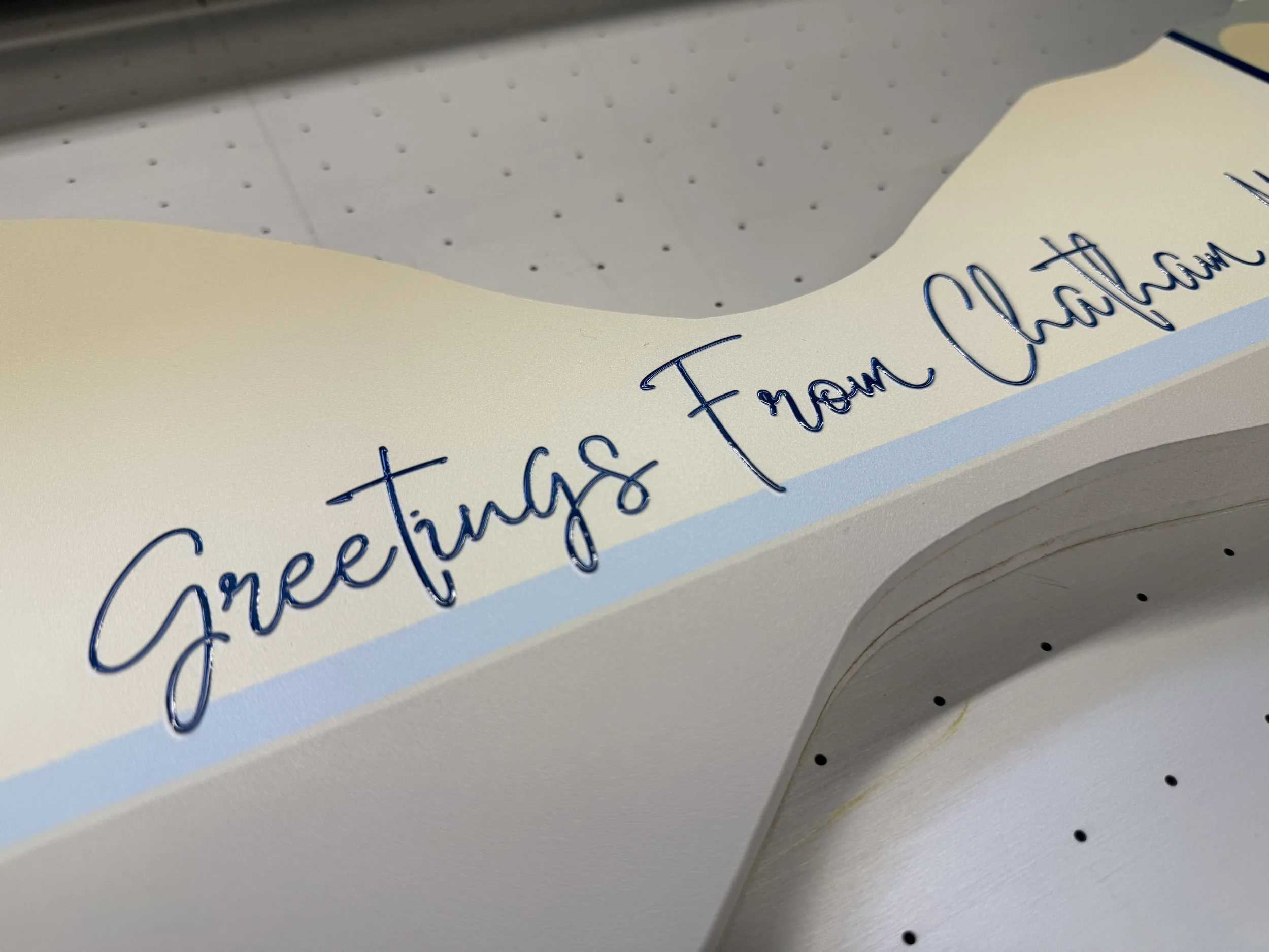 Close-up of a decorative paper with cursive writing, featuring the words 'Thank You' in blue ink, and a light blue border. The paper has a scalloped edge, and part of a dotted gray surface is visible in the background.