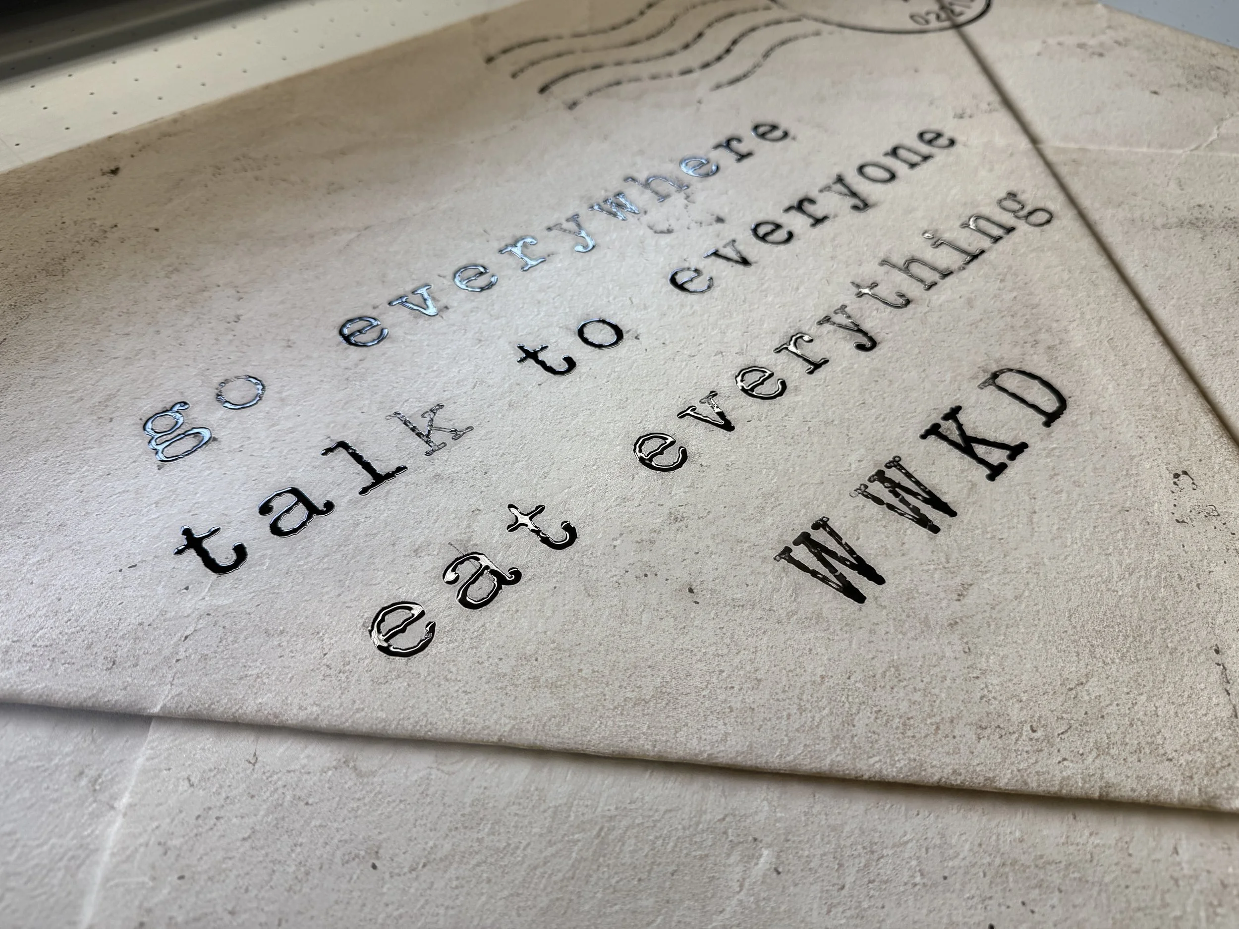 Close-up of engraved text and a logo on a light-colored, textured surface, possibly stone or concrete.