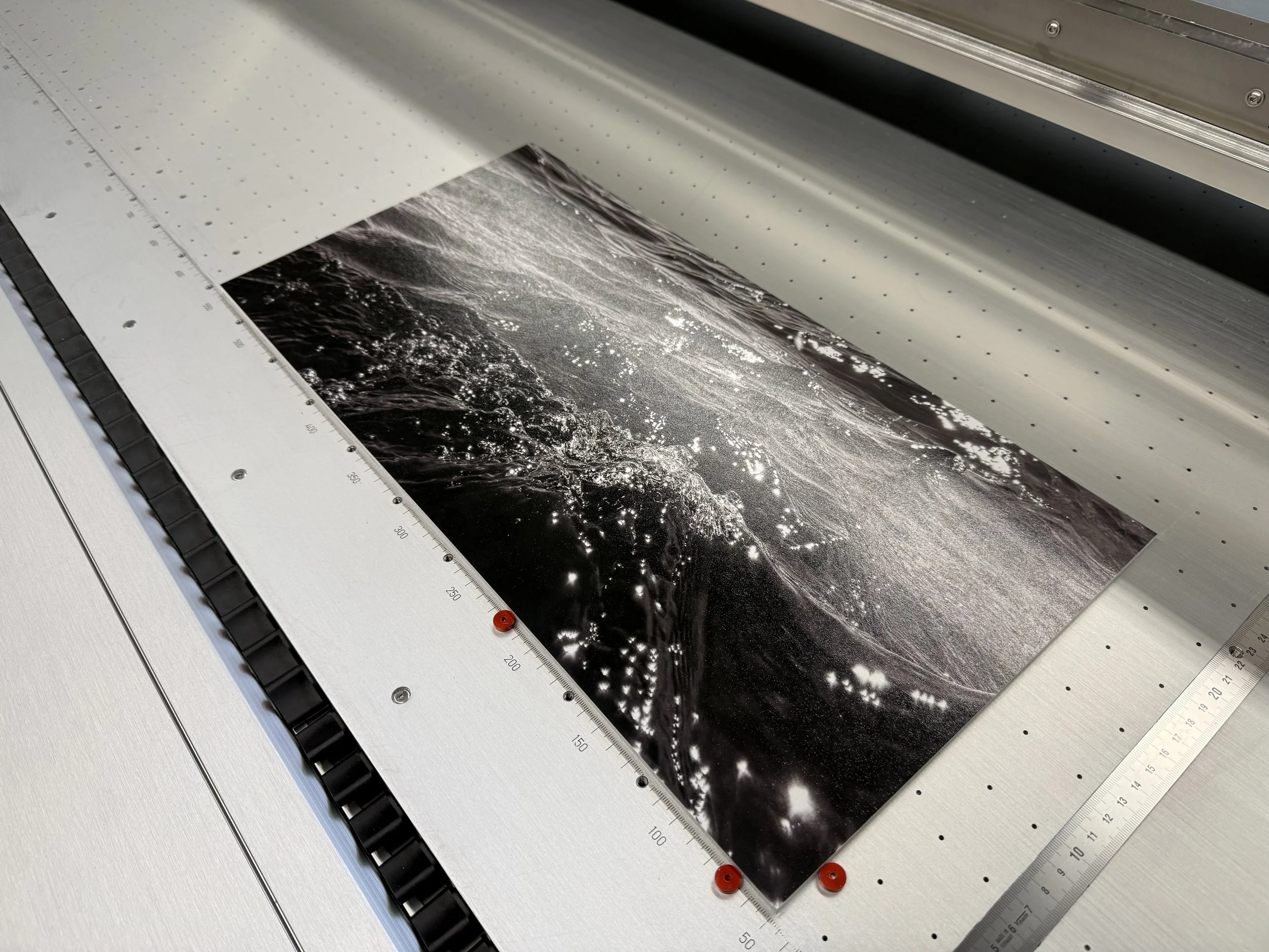 A large-format printer printing a black-and-white photograph of water with bubbles and splashes, using a precise measurement guide along the edge.