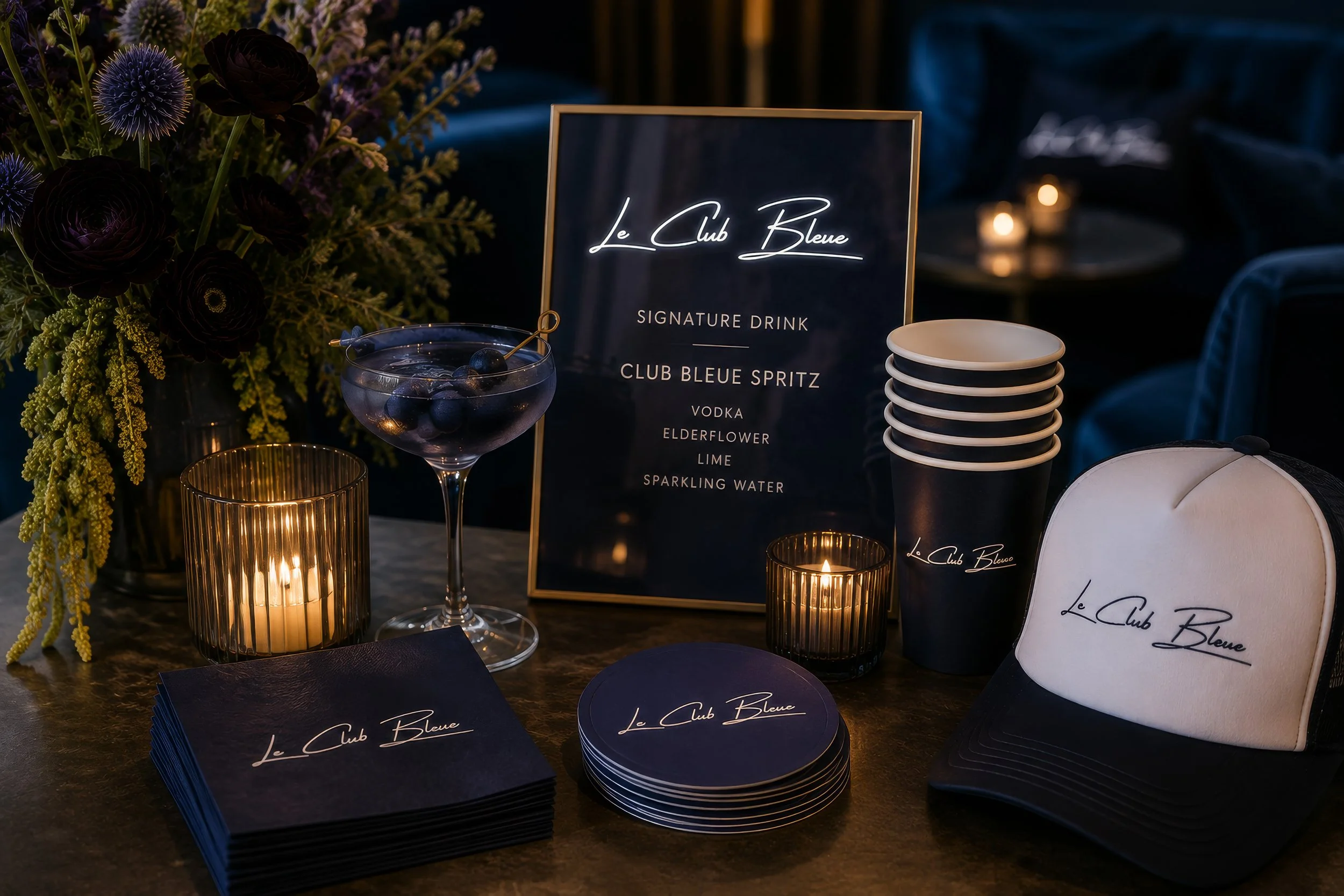 Personalized party décor featuring a signature cocktail sign, custom paper cups, cocktail napkins, branded trucker hat, candles, florals, and coordinated event styling for an unforgettable celebration.