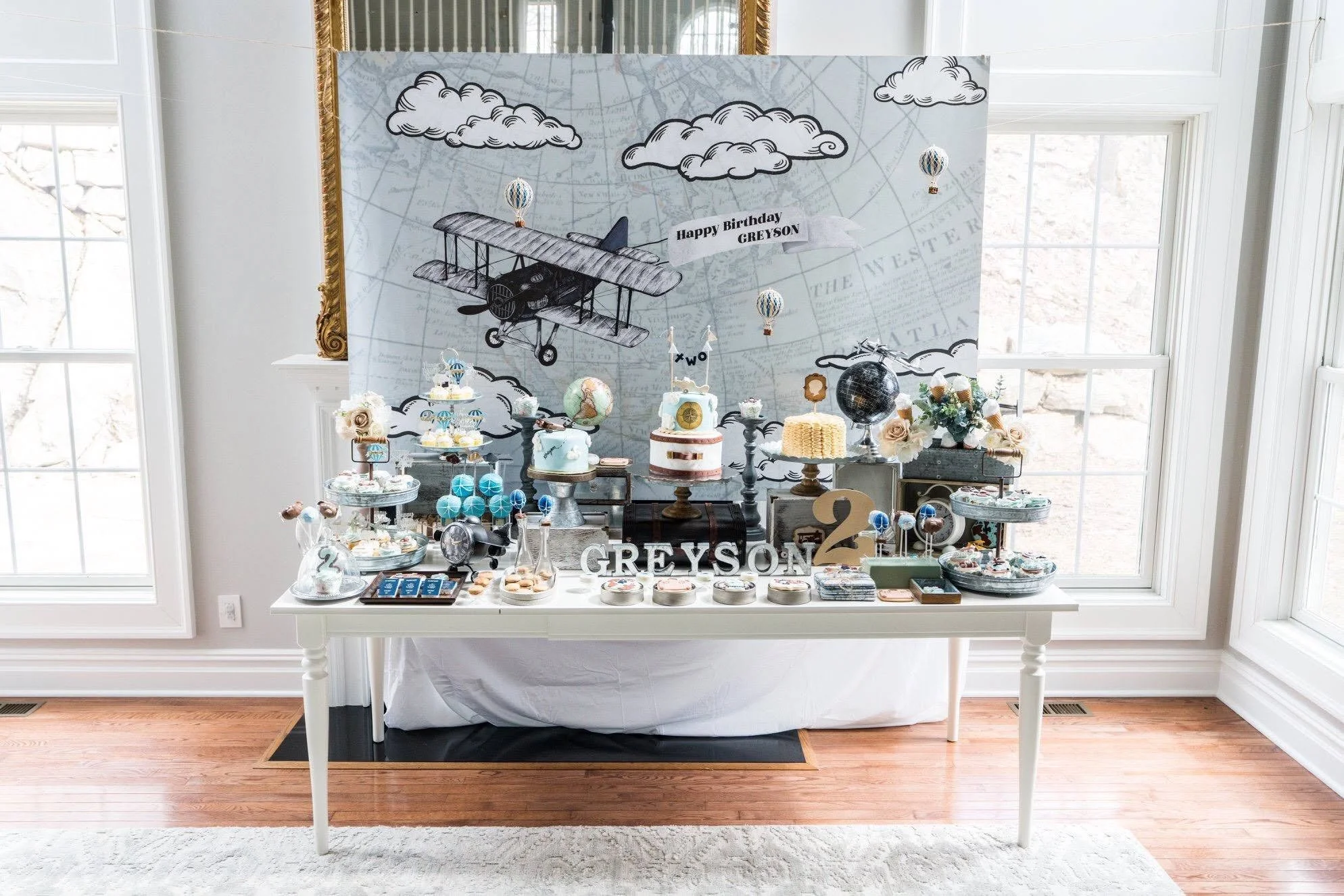 Vintage airplane-themed second birthday dessert display featuring custom illustrated backdrop, aviation-inspired event branding, hot air balloon details, and coordinated signage for an adventurous celebration.