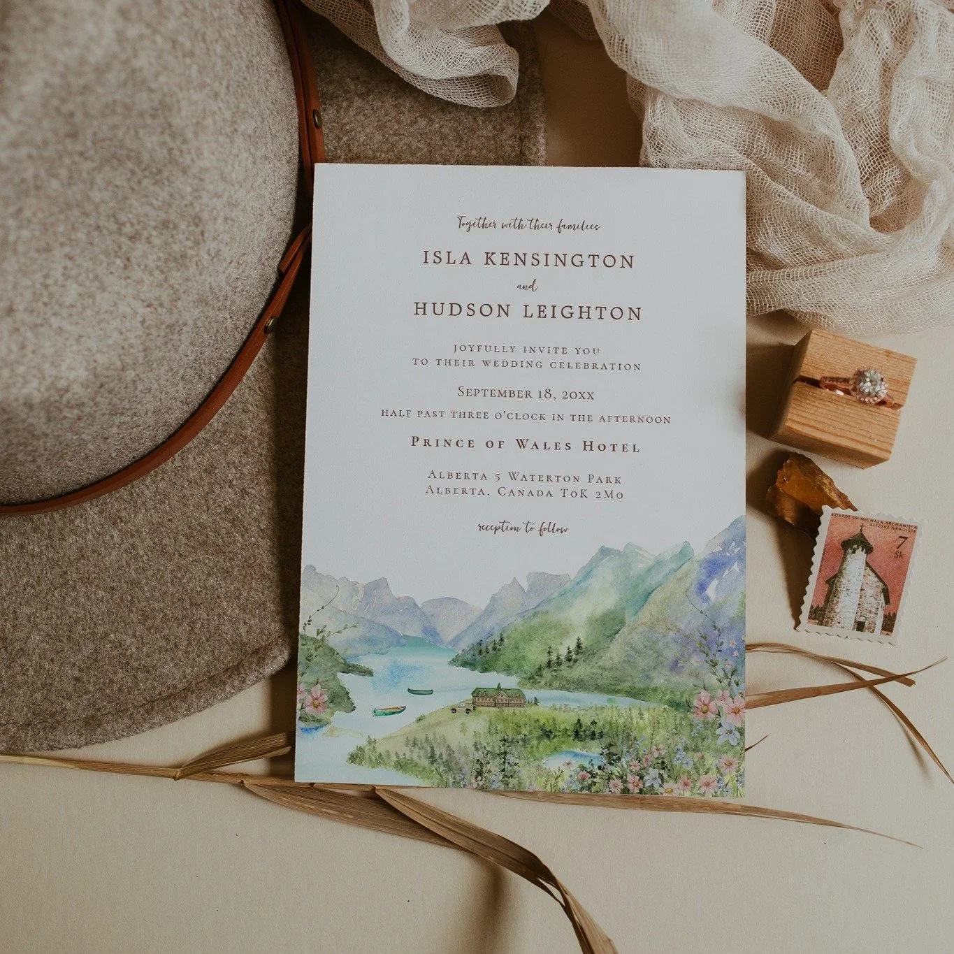Custom watercolor wedding invitation featuring a hand-painted Waterton Park mountain landscape styled with a ring box, vintage postage, and wedding details.