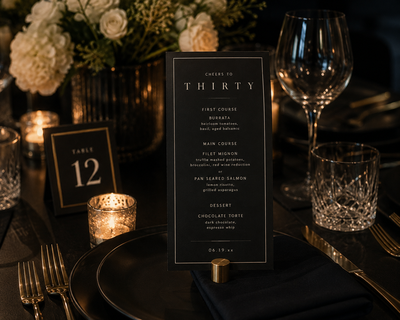 Moody black and gold 30th birthday tablescape featuring an elegant dinner menu, table number, candlelight, crystal glassware, and white florals.