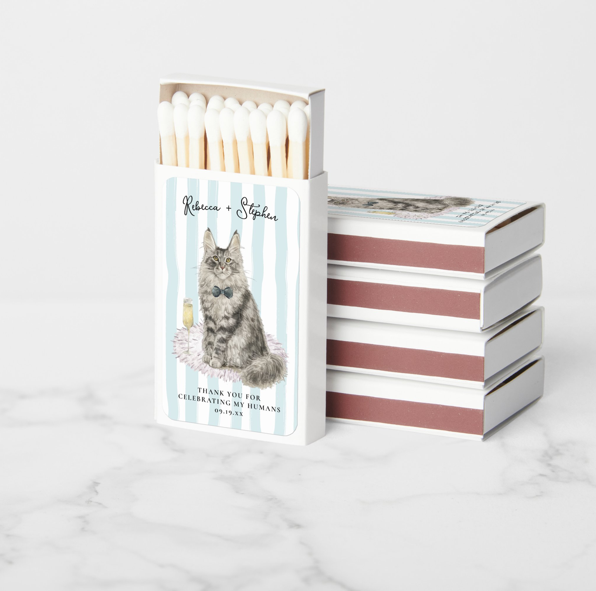 Personalized wedding favor matchboxes featuring a hand-painted watercolor portrait of a Maine Coon cat in a bow tie with the couple's names and wedding date, created as custom pet wedding favors for guests.