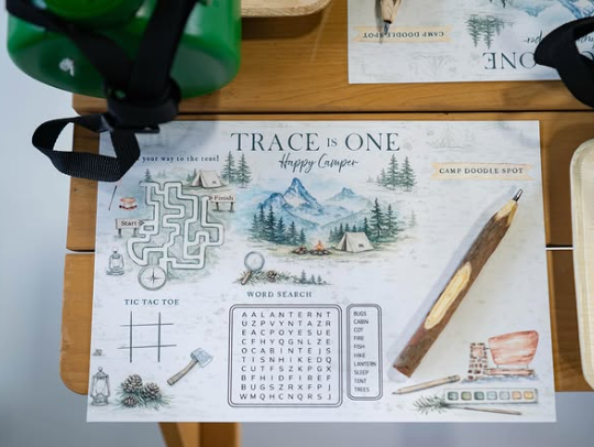 Close-up of a custom illustrated children's activity placemat featuring watercolor camping artwork, games, puzzles and personalized branding created for the Camp T.K. birthday celebration.