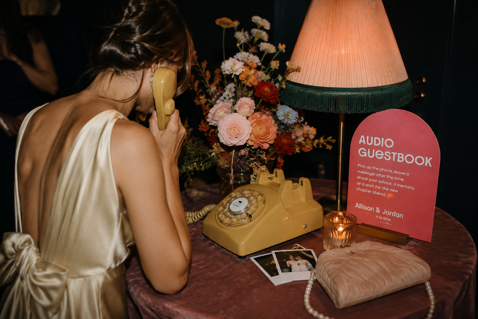 Wedding guest leaving a message on a vintage rotary audio guestbook surrounded by colorful florals, candlelight and playful reception signage.