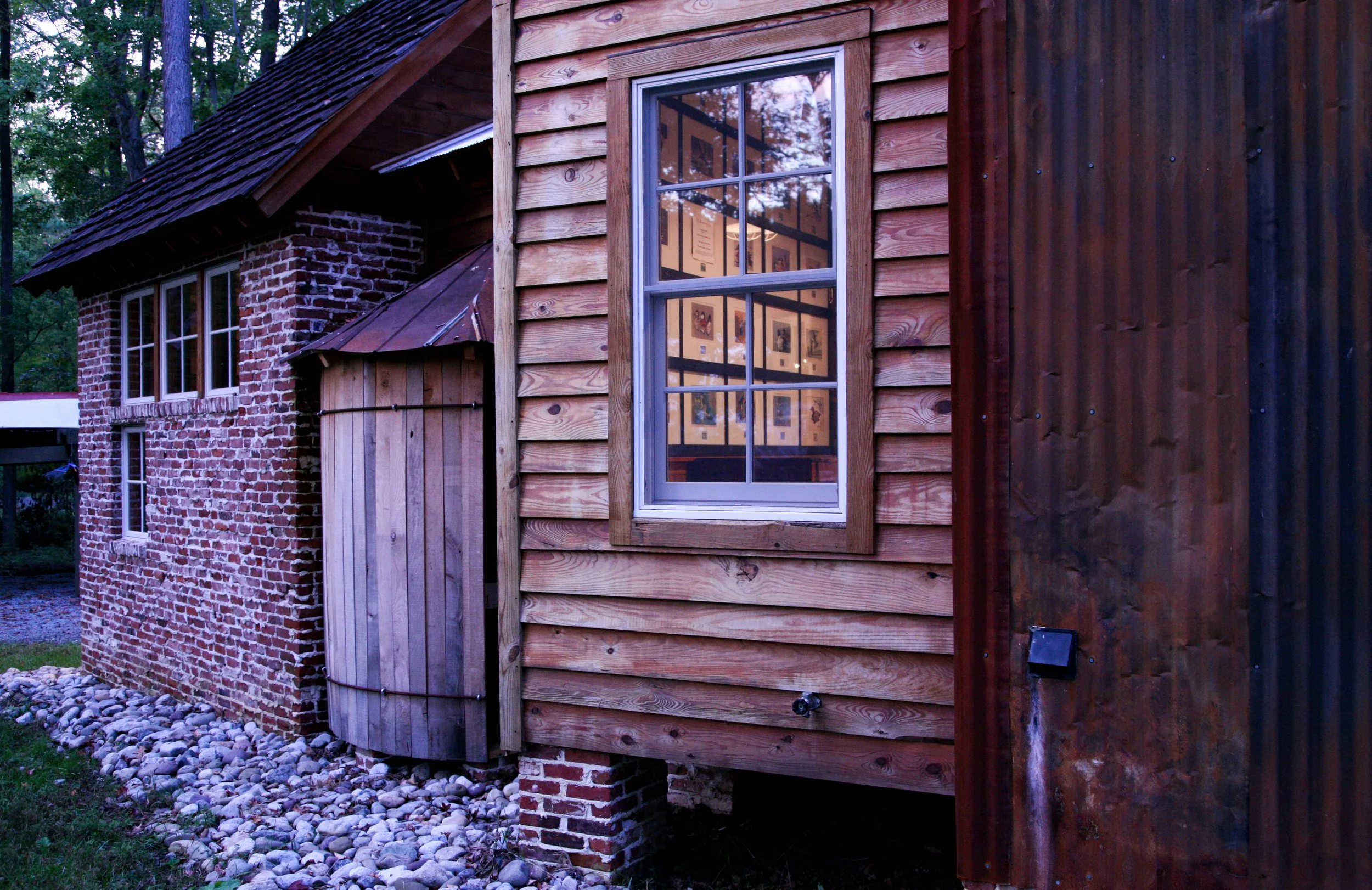 Rustic cabin exterior with brick and wood paneling, window reflecting interior decor, set amidst a wooded area.