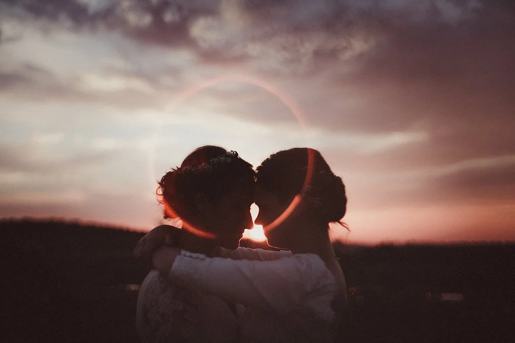 Un couple s'embrassant lors d'un coucher de soleil, avec une éclipse solaire partielle et un cercle lumineux derrière eux.