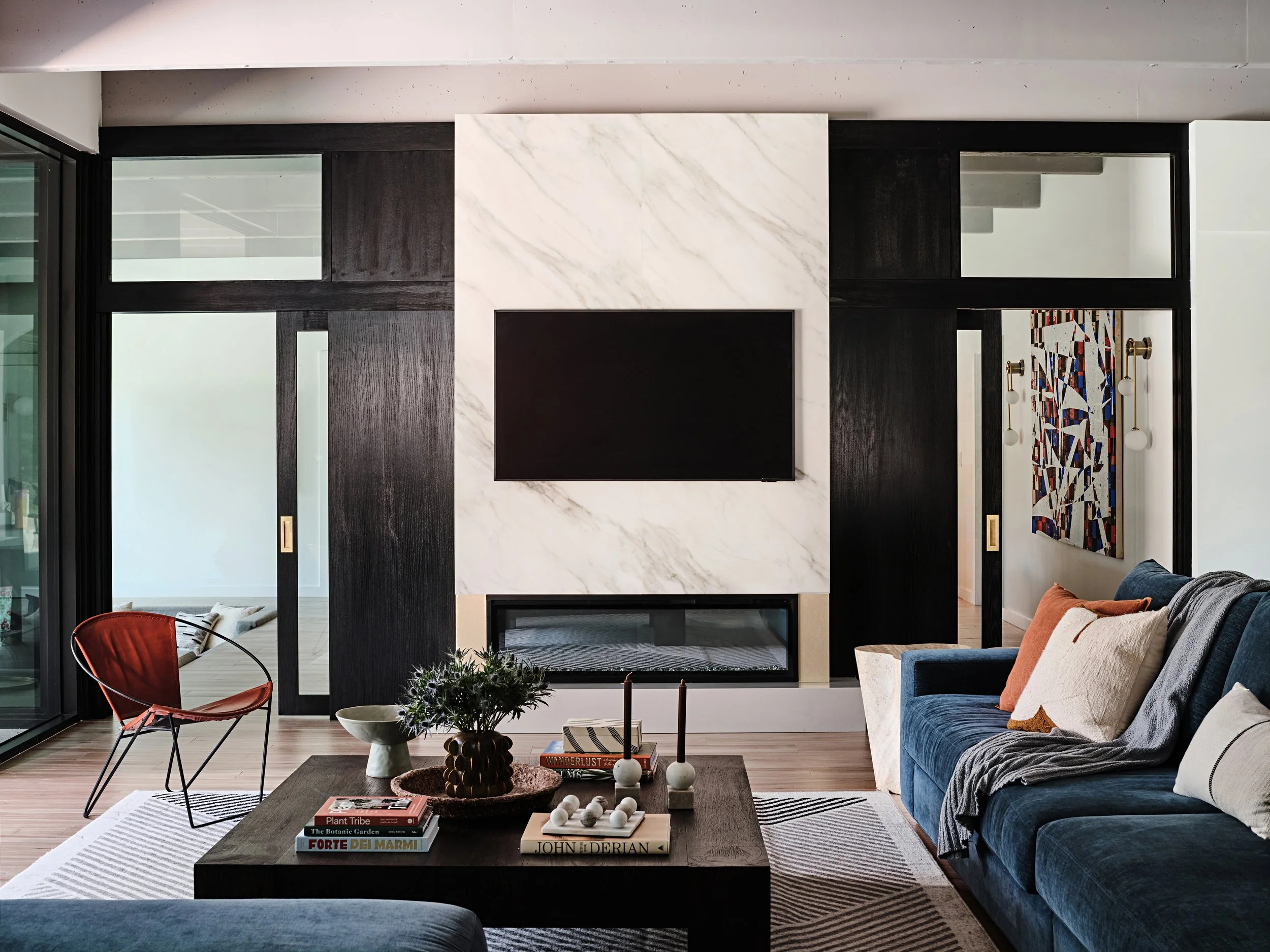 Custom designed fireplace and tv wall wrapped in stone. Electric fireplace with brass details. Large sliding glass and black wood doors in Miami, Fl home. Interior design by Concept 2 Design.