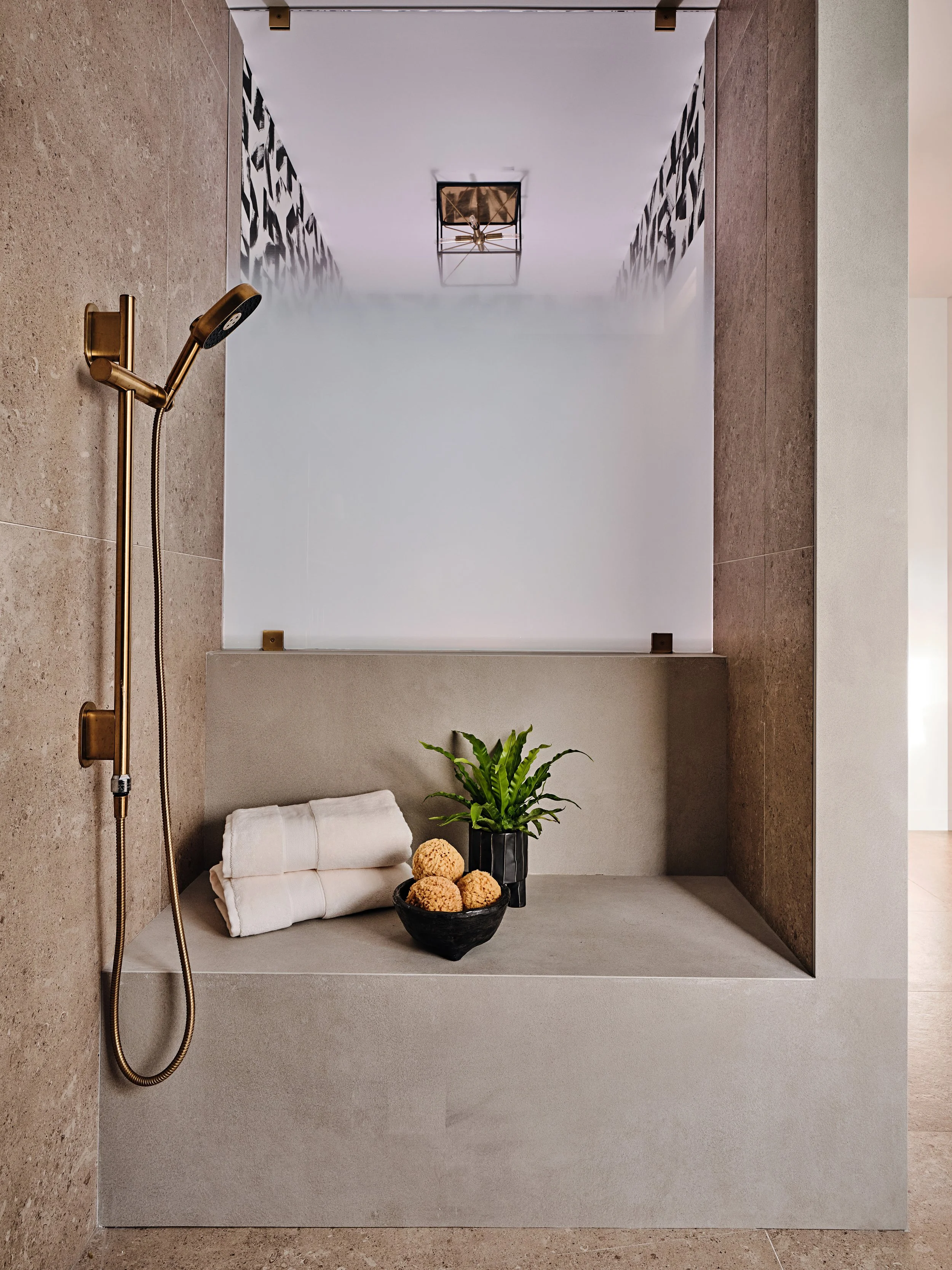 Bench in bathroom. Hand shower and brass fixtures. Primary bathroom in South Florida new construction home. Interior design by Concept 2 Design