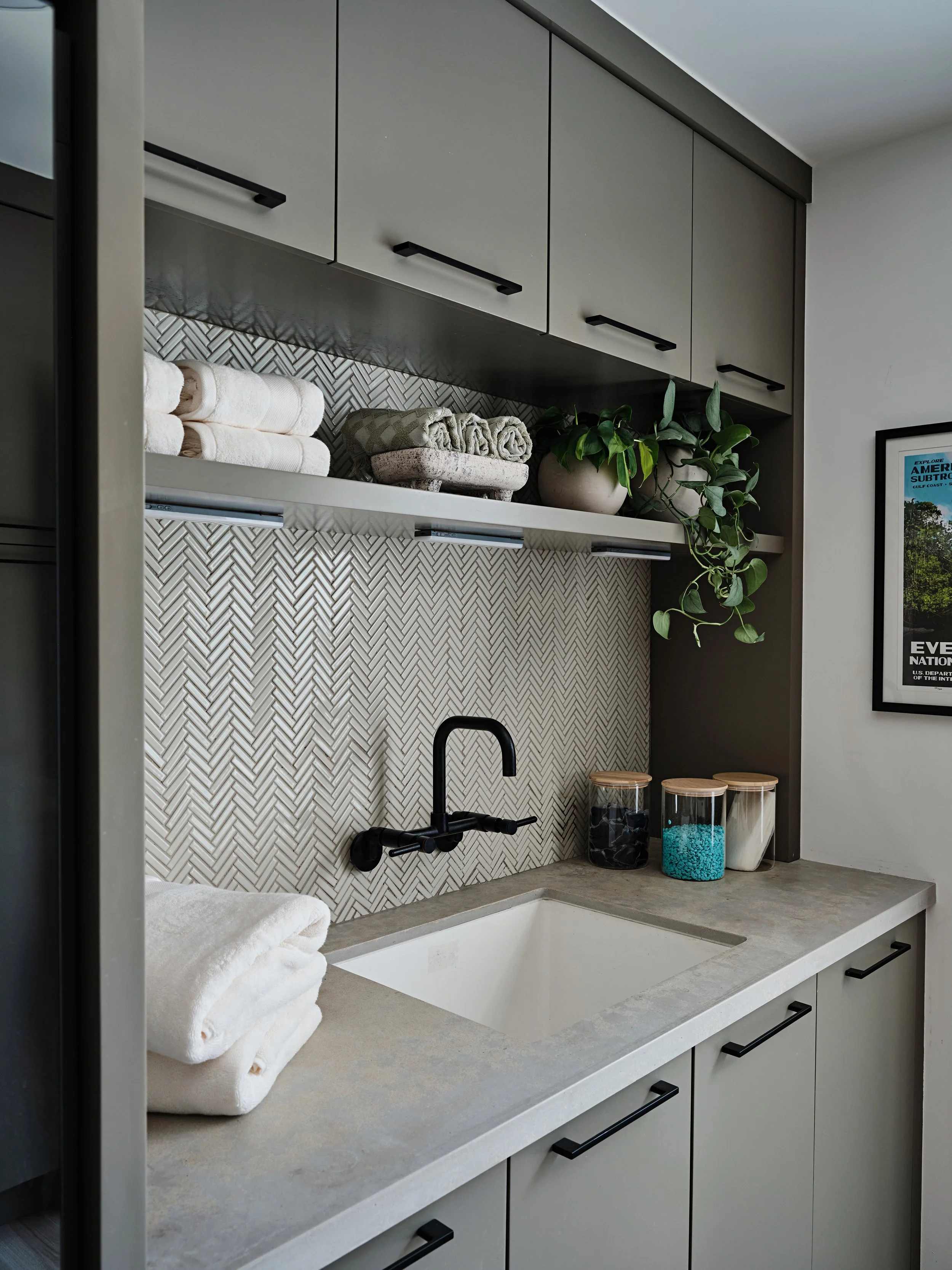Wall mounted black faucet in laundry room. Quartz countertops and custom built in cabinetry in khaki color. Interior design by Concept 2 Design.