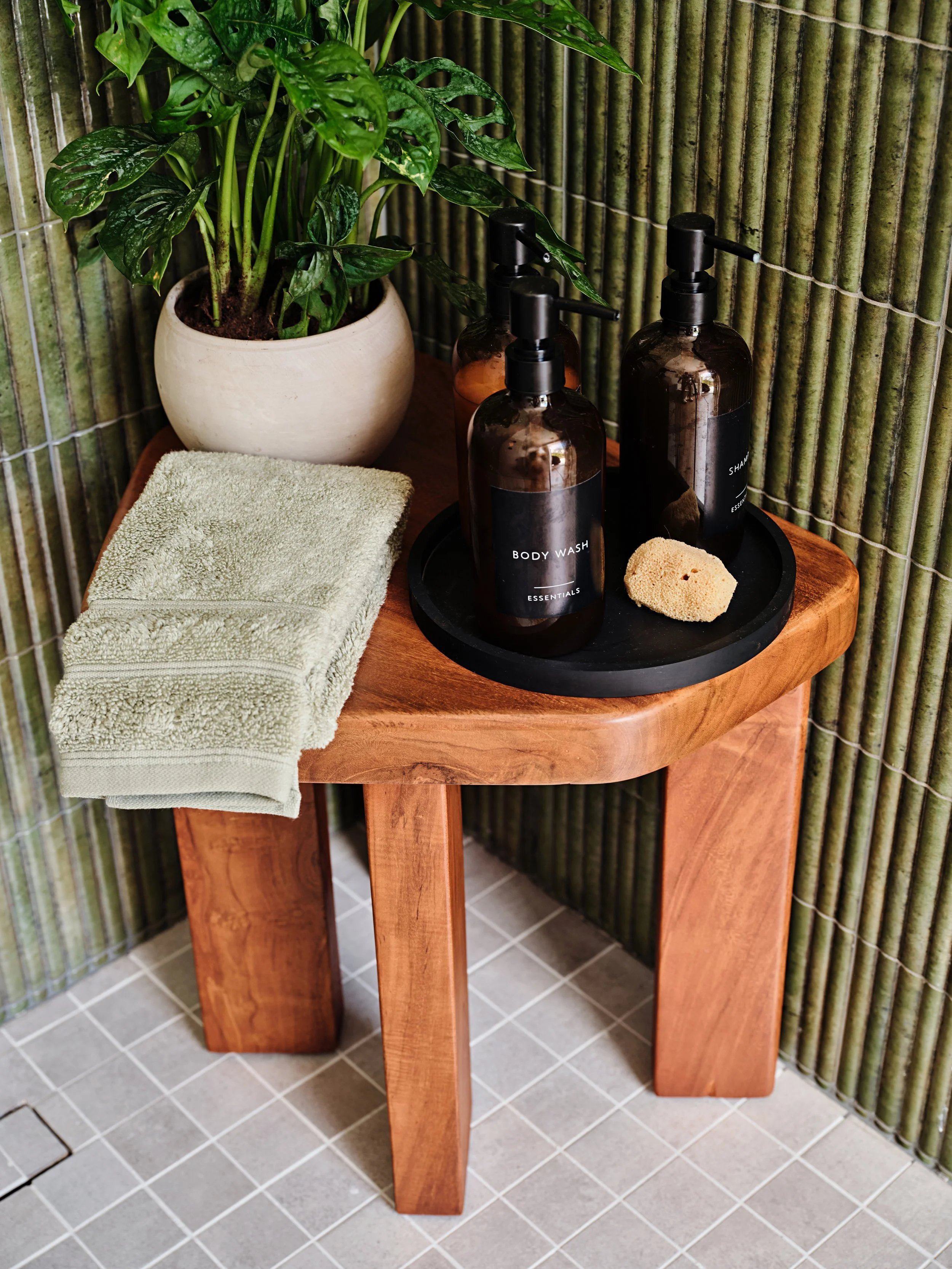 Green wall tile in Cabana bathroom. Teak stool in shower. Amber shampoo bottles in a new construction residence in Miami, Fl. Interior design by Concept 2 Design.
