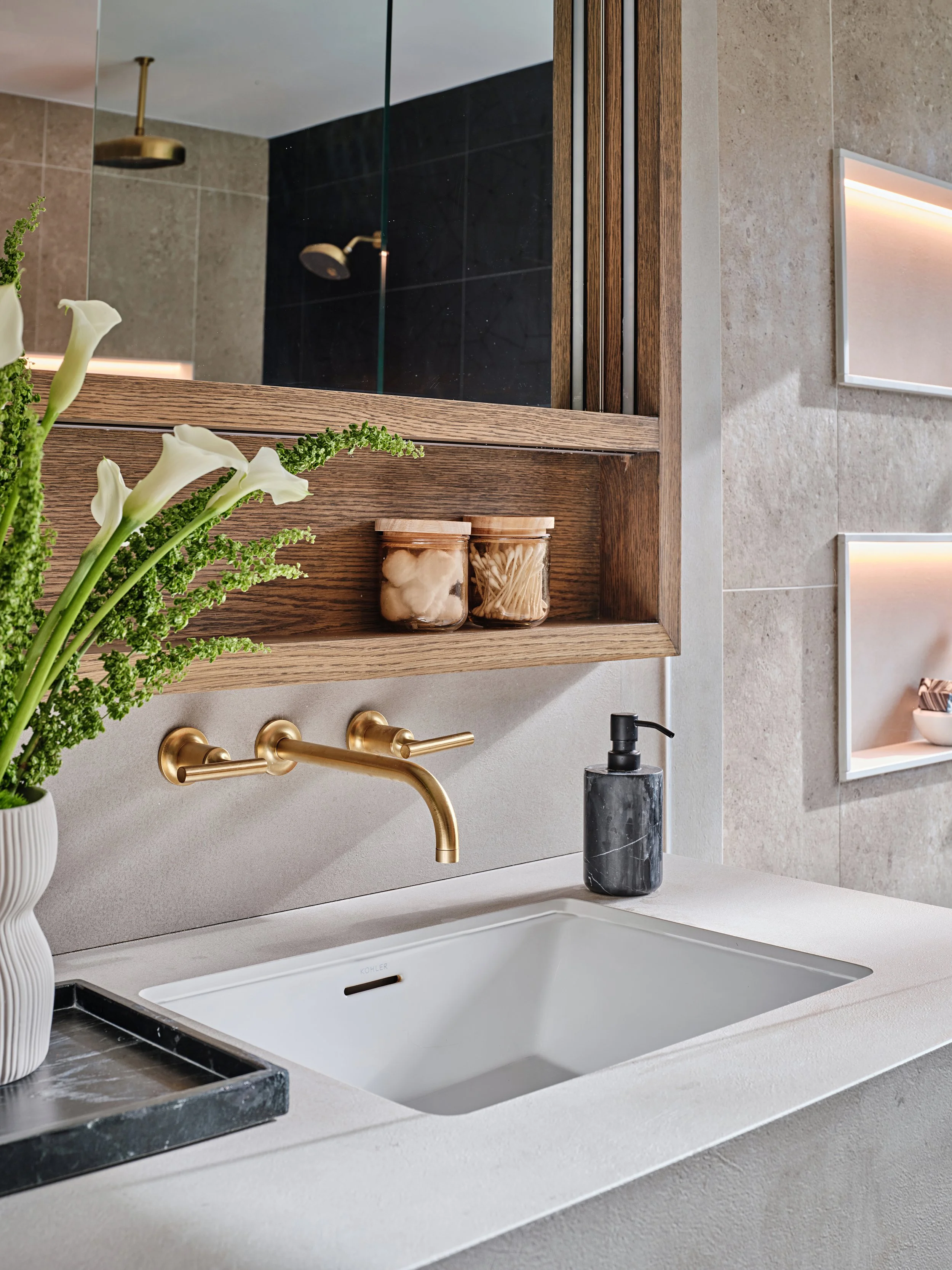 Brass wall mounted faucets in primary bathroom for a new construction home in South Florida. Concrete like quartz countertops. Interior design by Concept 2 Design.