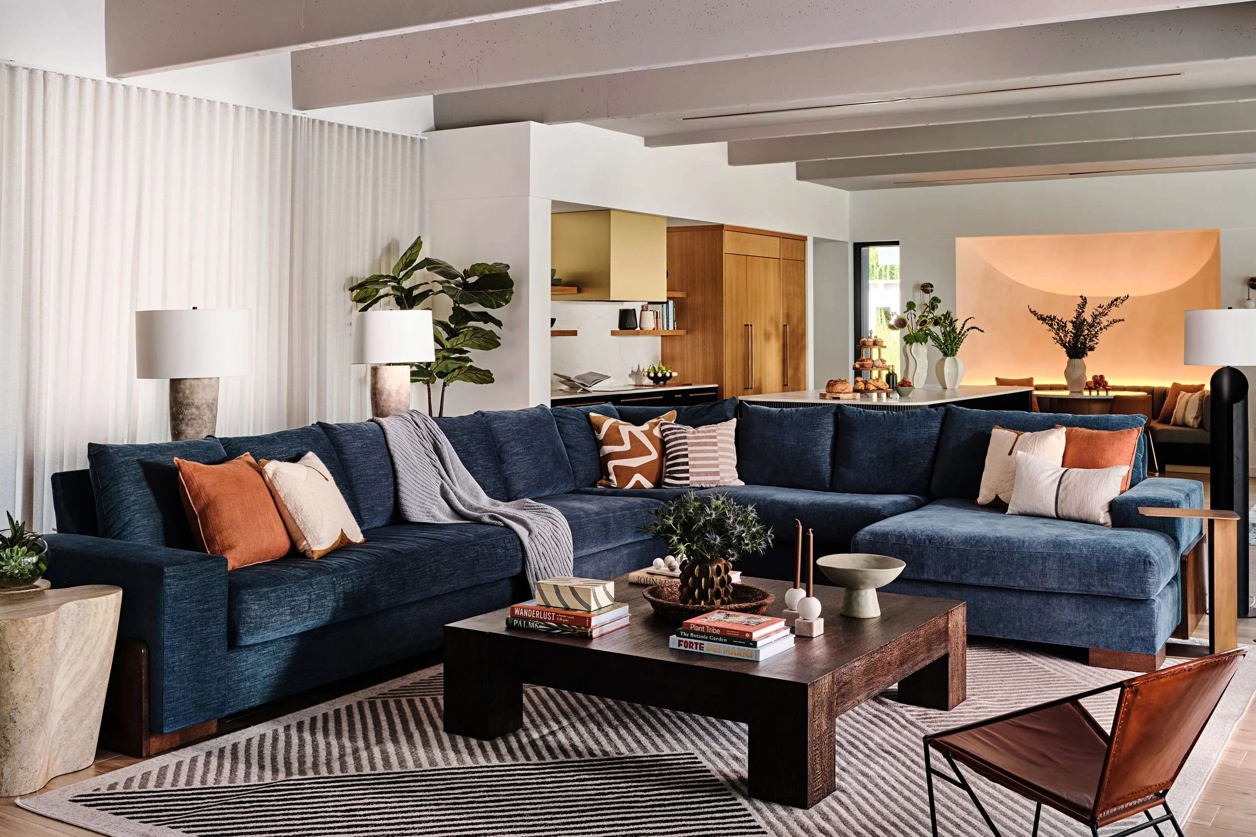 Navy blue sectional with copper and brown accent pillows in a family room in Miami, Fl. Black patterned area rug and chunky coffee table. Interior design by Concept 2 Design. 
