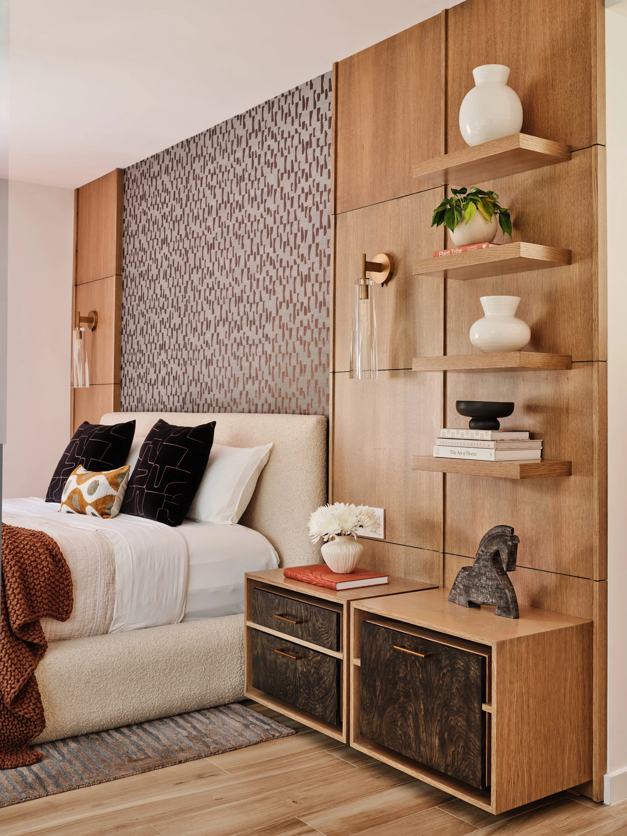 Wallpaper behind bed. Custom built in nightstand cabinetry. Burlwood doors. Open shelving with accessories. Brass wall sconces. Interior Design by Concept 2 Design