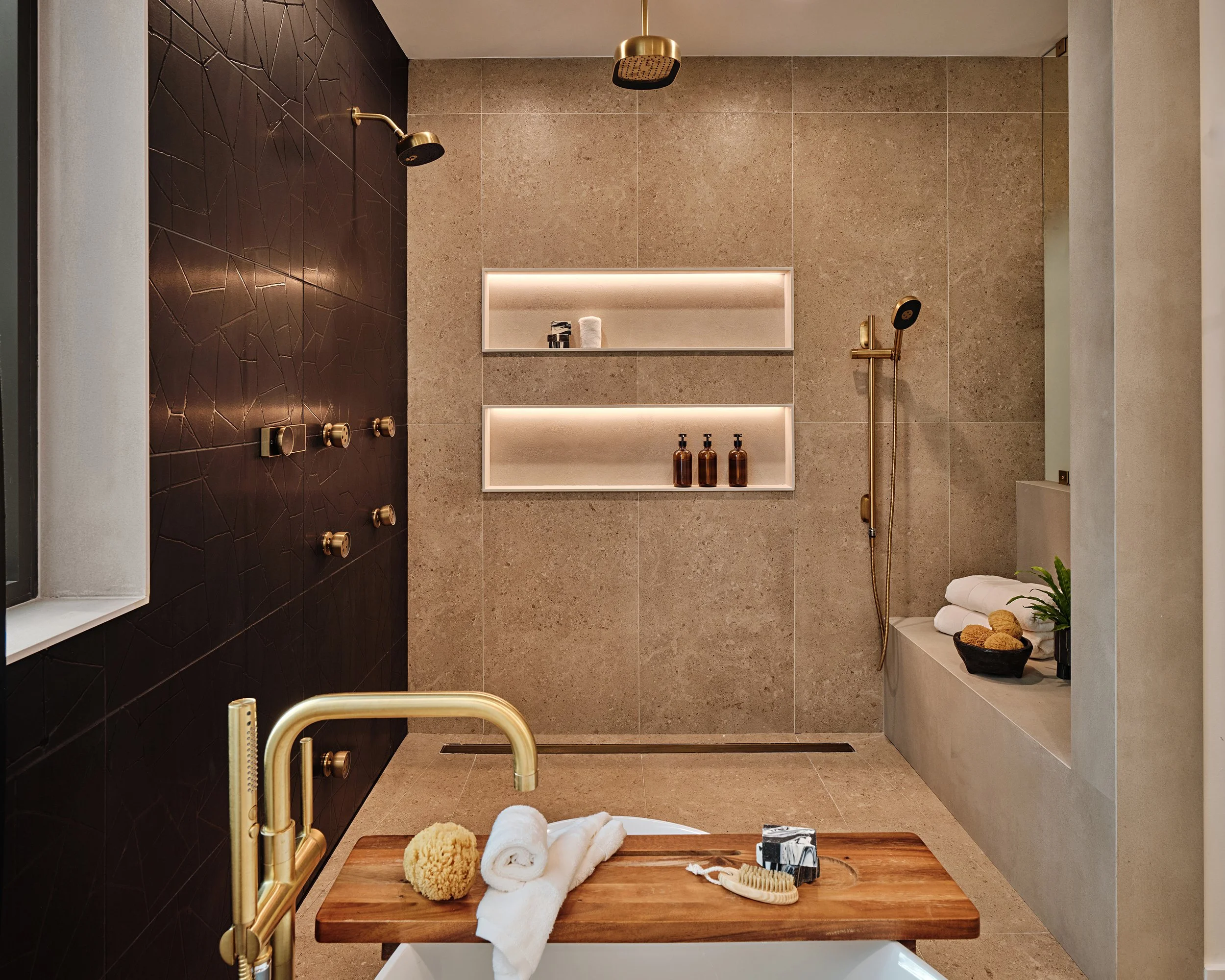 Moody bathroom with LED lighting in bathroom niches. Brass shower fixtures. Freestanding bathtub. Interior design by Concept 2 Design.
