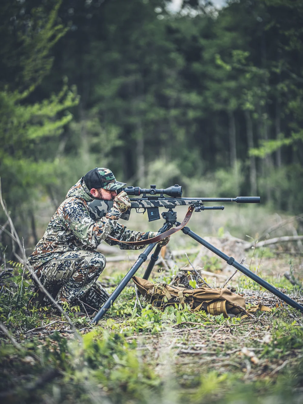 Shooter prone with a suppressed rifle in the forest