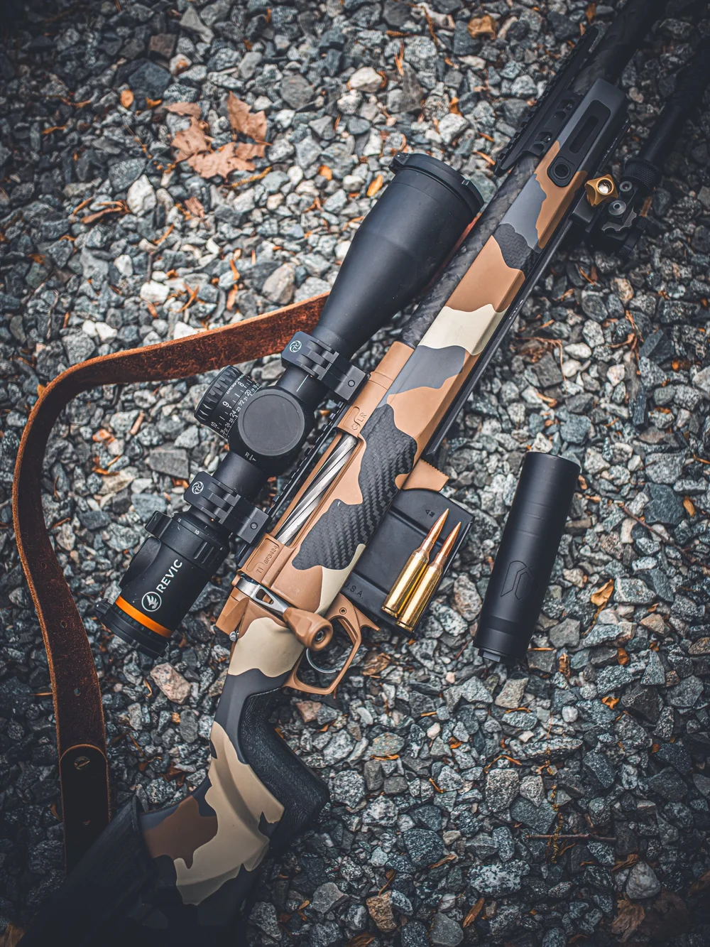 Camouflage-finished rifle and suppressor on gravel