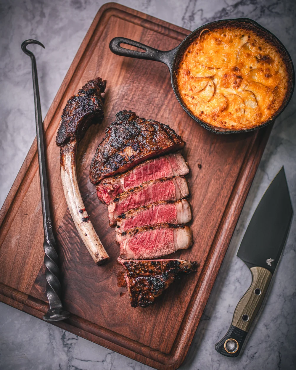 Sliced ribeye on a wood board with knife and skillet