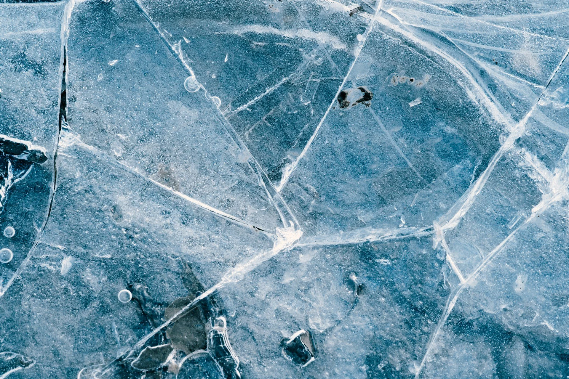 A top-down close-up of thick, crystalline blue ice with deep cracks and air bubbles trapped beneath the surface, illustrating the limits of fragmented systems.
