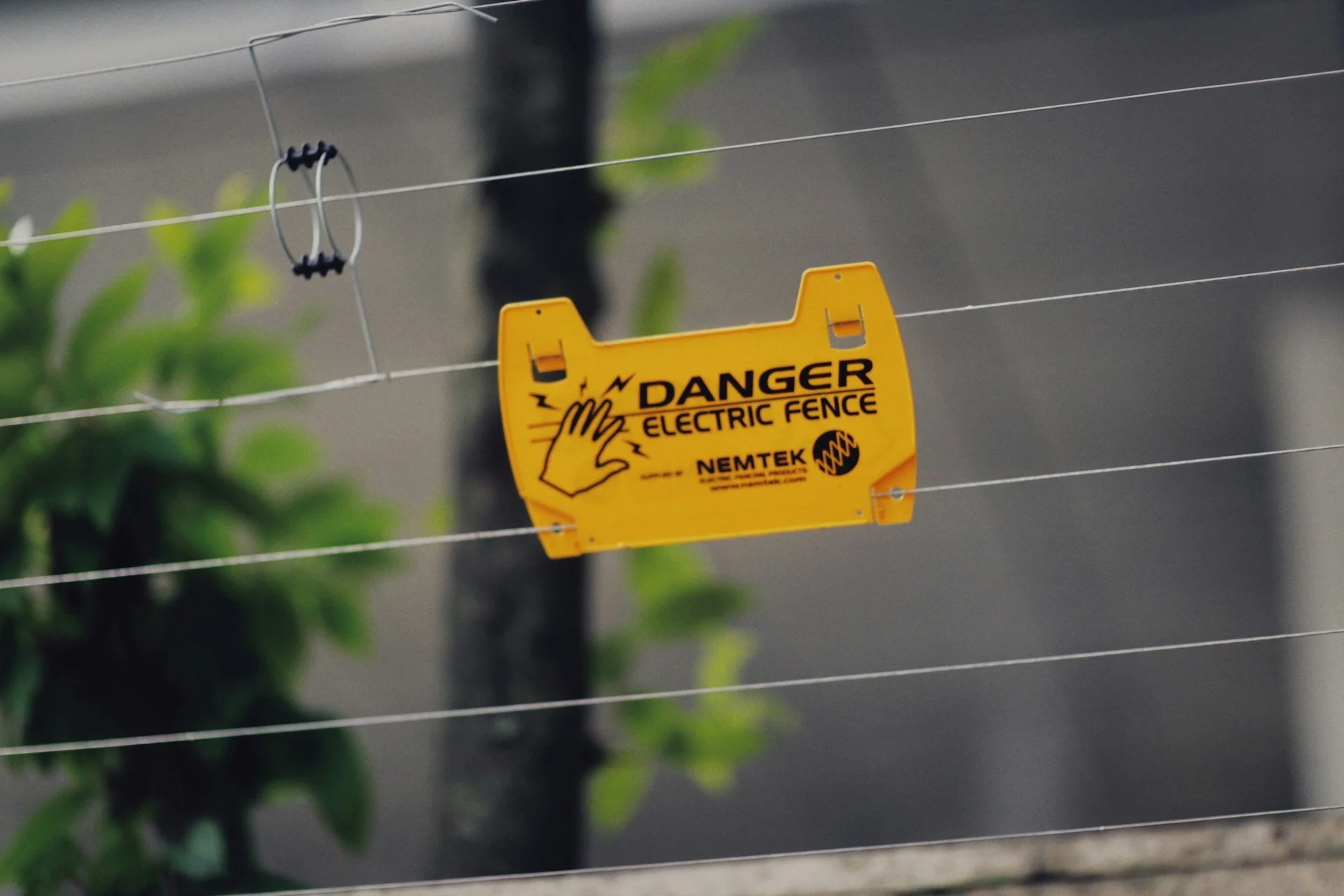 Electric fence warning sign symbolizing Jurassic Park author Michael Crichton’s concerns about biotechnology systems, commercialization, and scientific control.