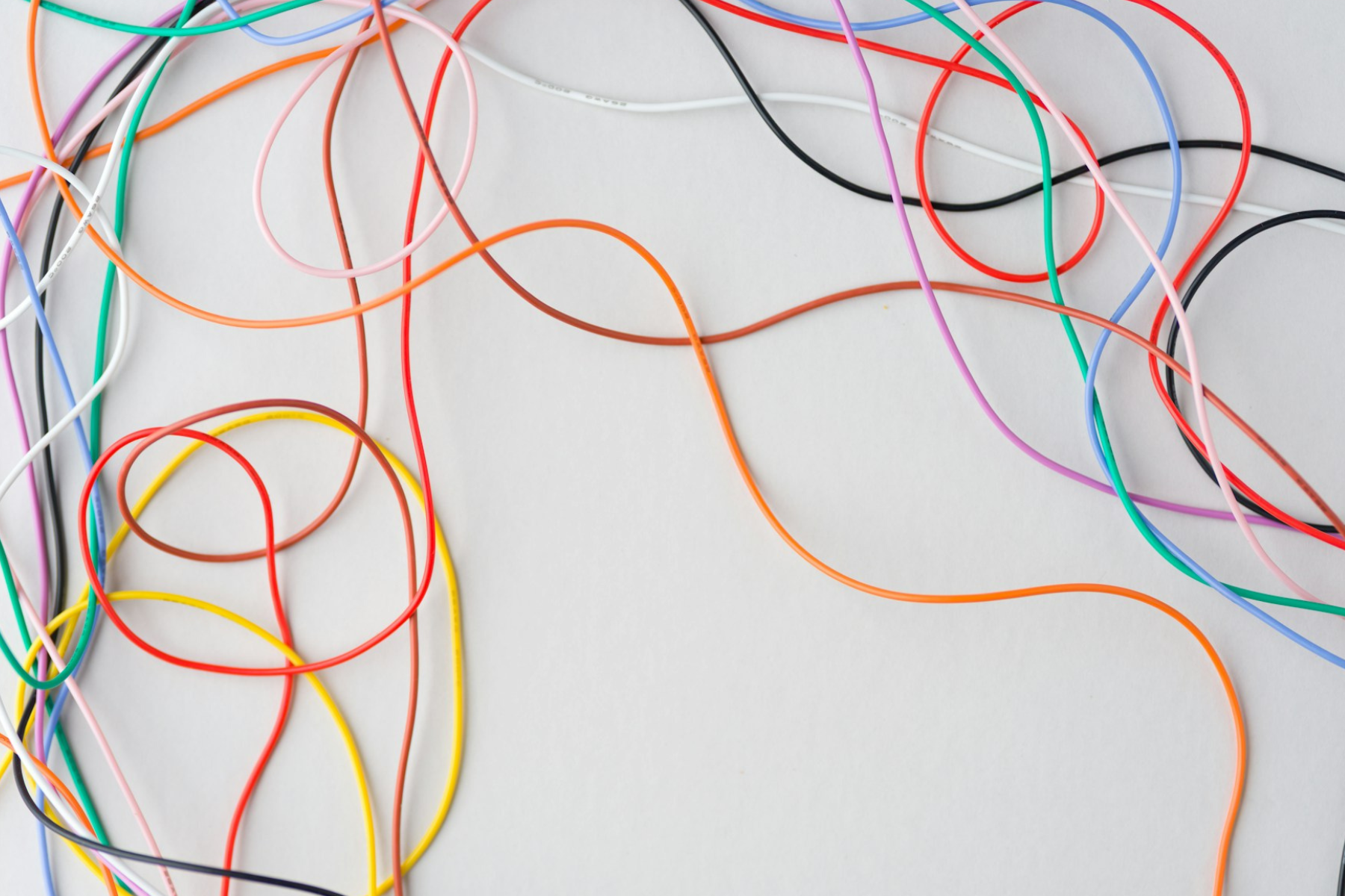 Close up of tangled multicolored electrical wires on a white surface, representing the complex neural networks and integrated systems of artificial intelligence.