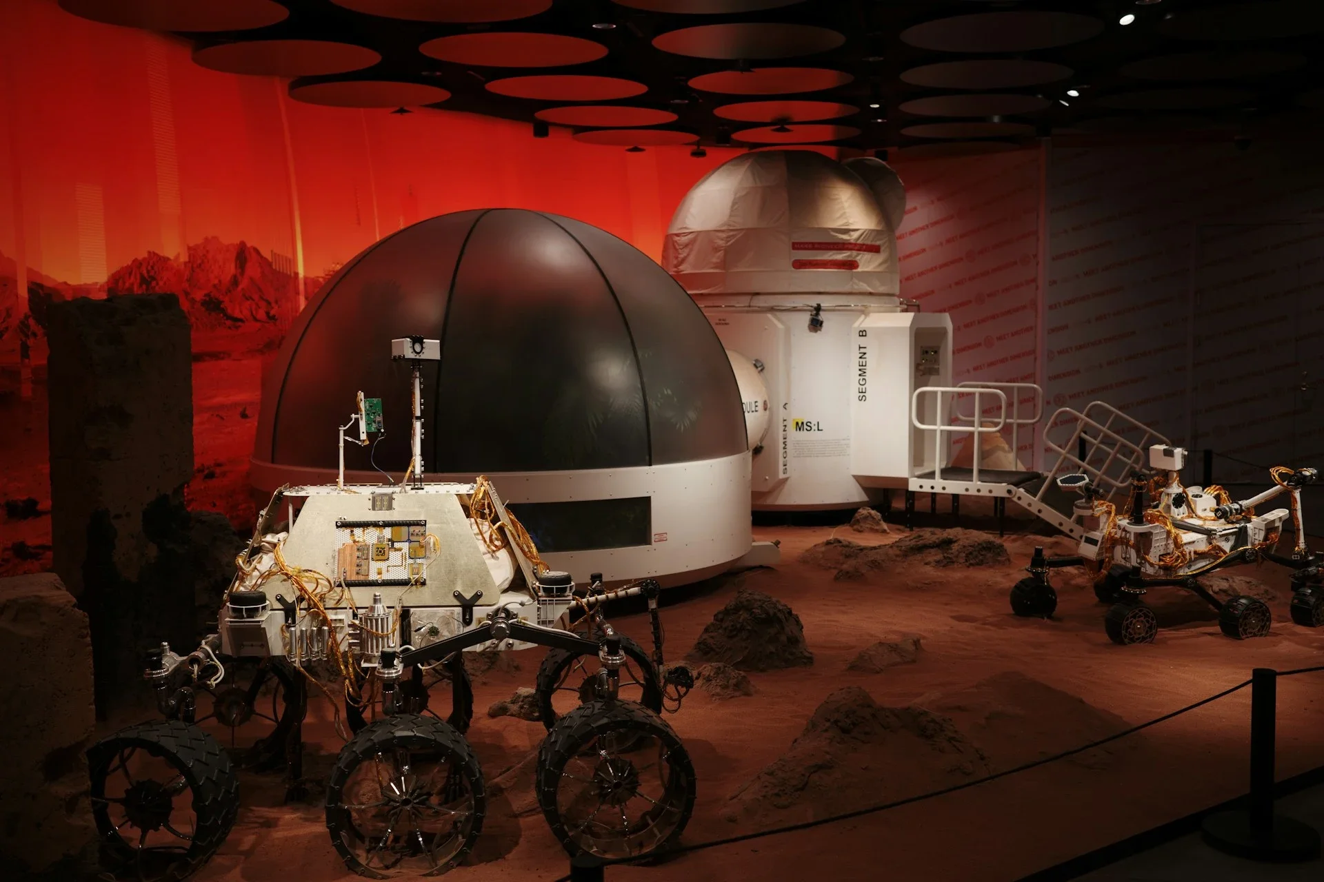 A museum exhibit showing a simulated Martian habitat and rovers on reddish terrain.