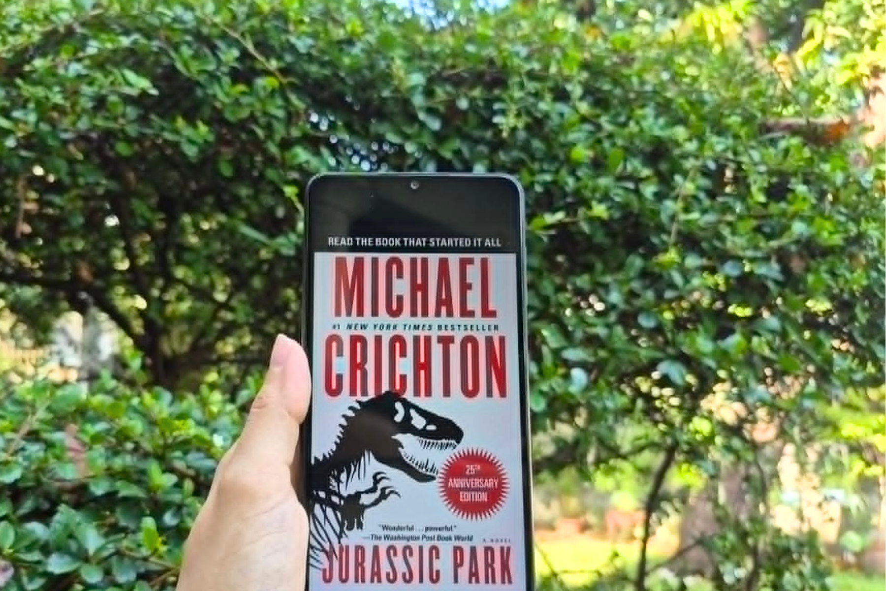 An e-book version of Michael Crichton’s Jurassic Park outdoors while reflecting on biotechnology, science fiction, and modern genetic engineering.