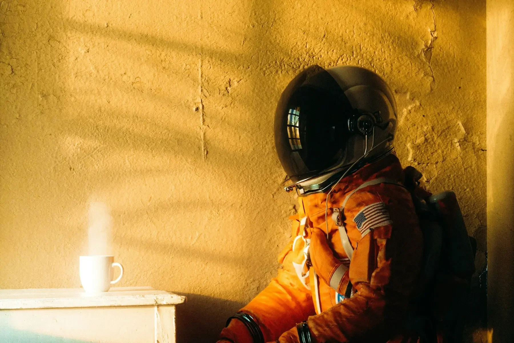 Astronaut sitting inside a Mars-like habitat beside a cup of hot water.