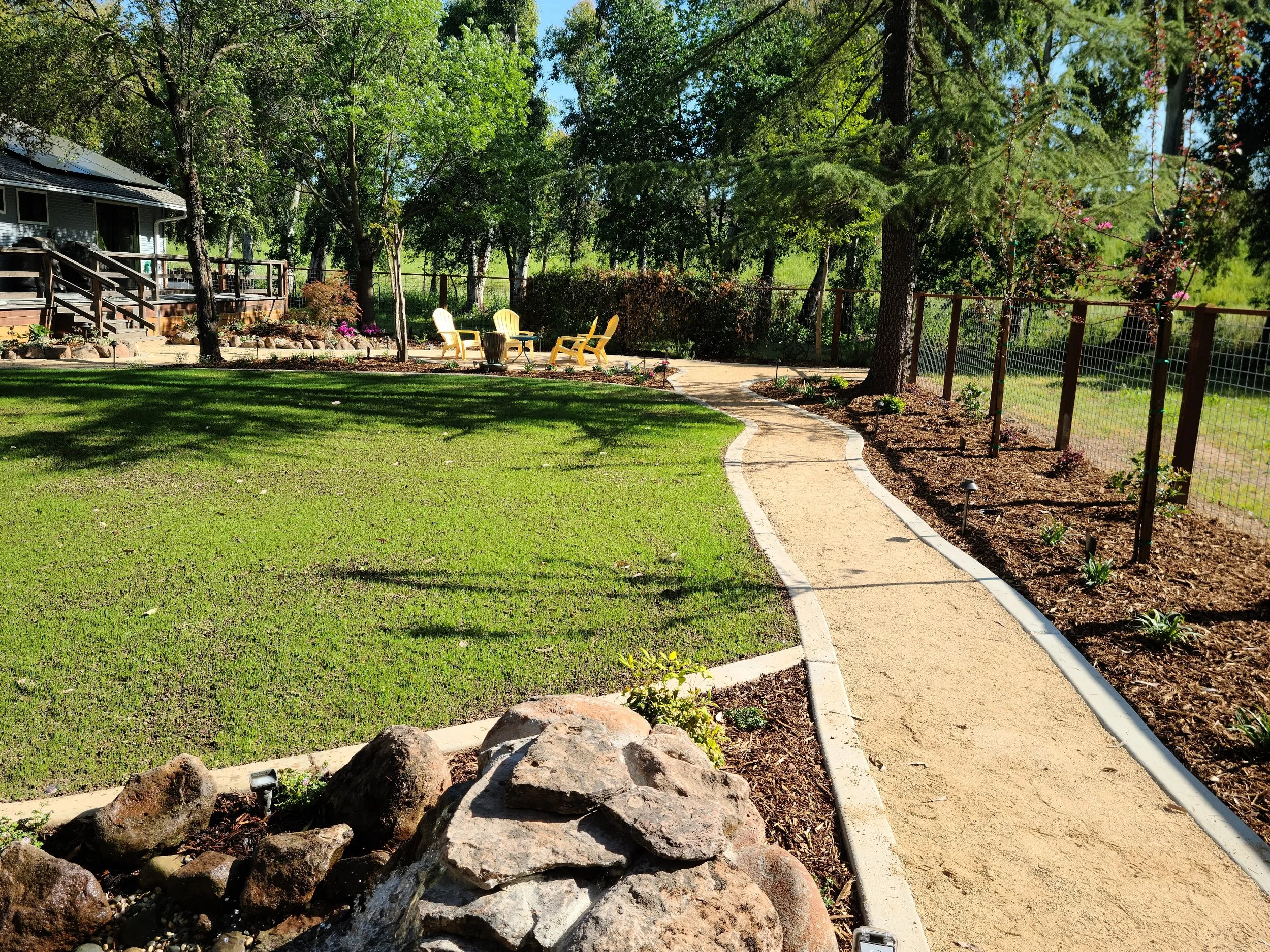 Large backyard with winding decomposed granite pathway, lawn, rock features, and fresh landscape beds.