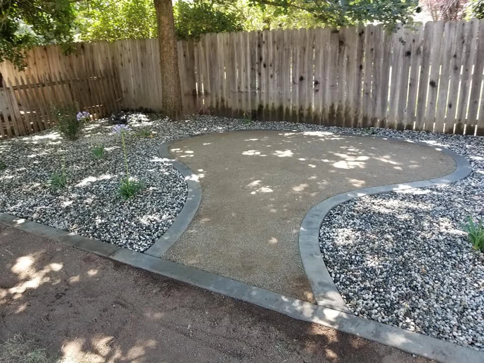 Landscaping Yuba City CA patio with decorative concrete, curved edging, and low-maintenance rock landscape.