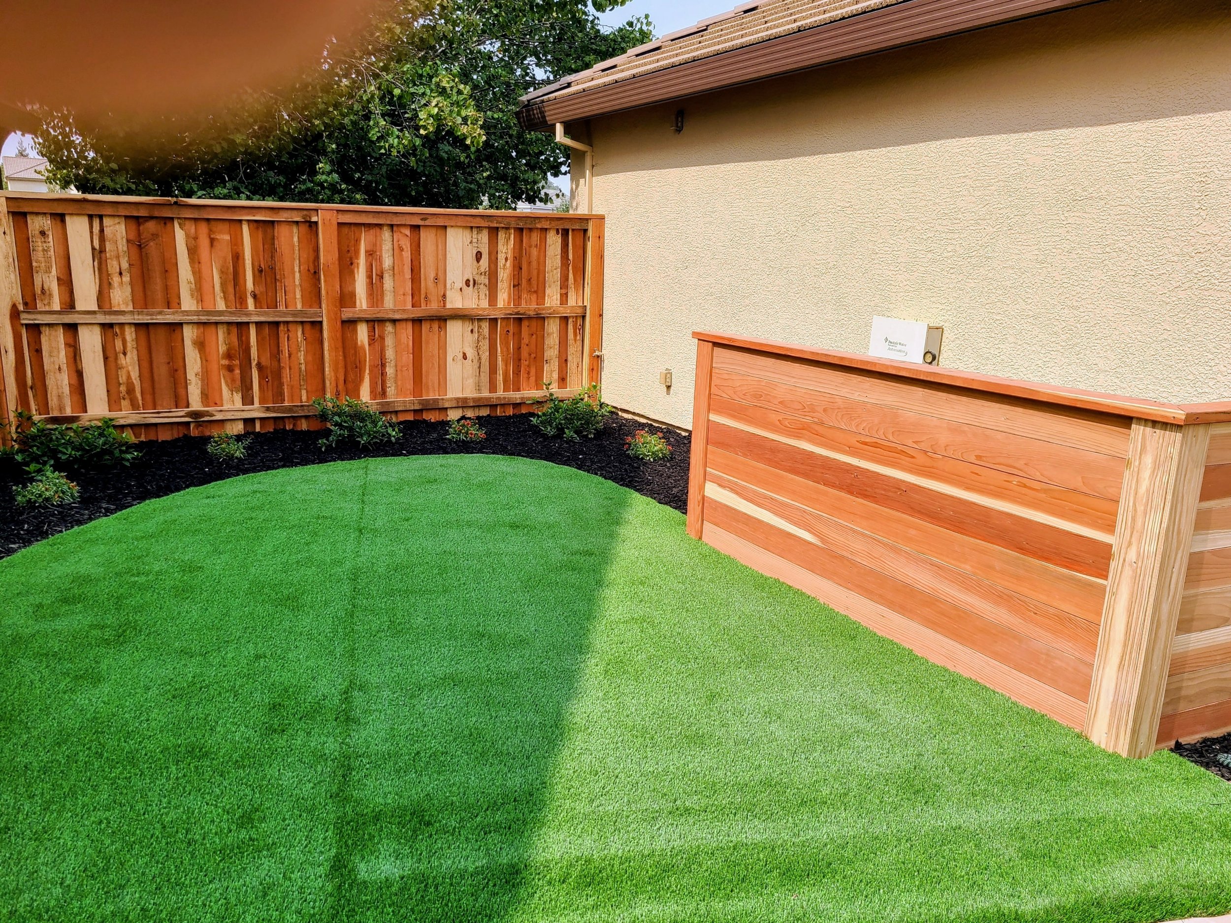 Landscaping Yuba City backyard featuring artificial turf, cedar planter, fresh mulch, and new landscape beds.