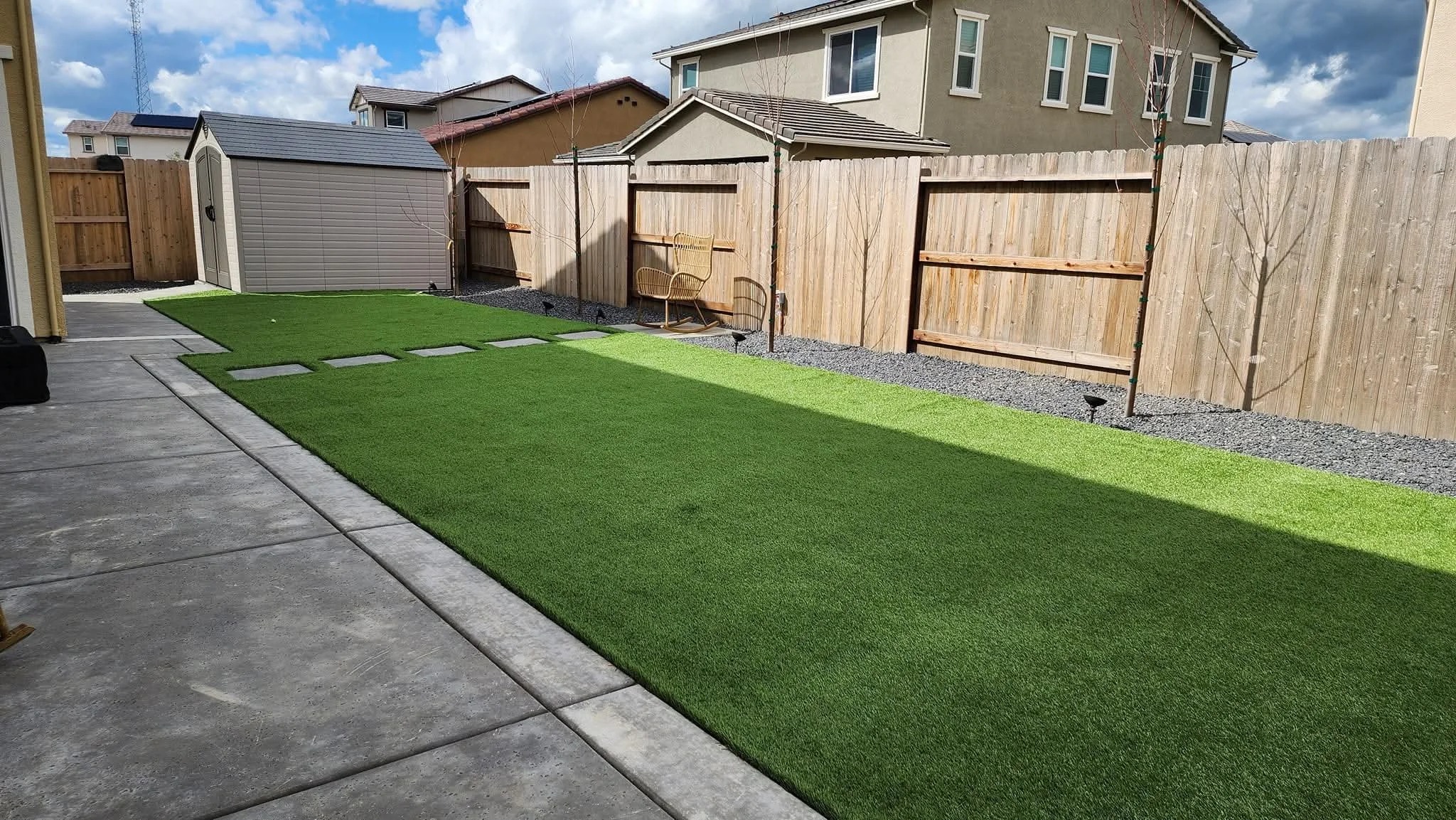 Modern backyard transformation with artificial turf, concrete patio, gravel borders, and stepping stone walkway.