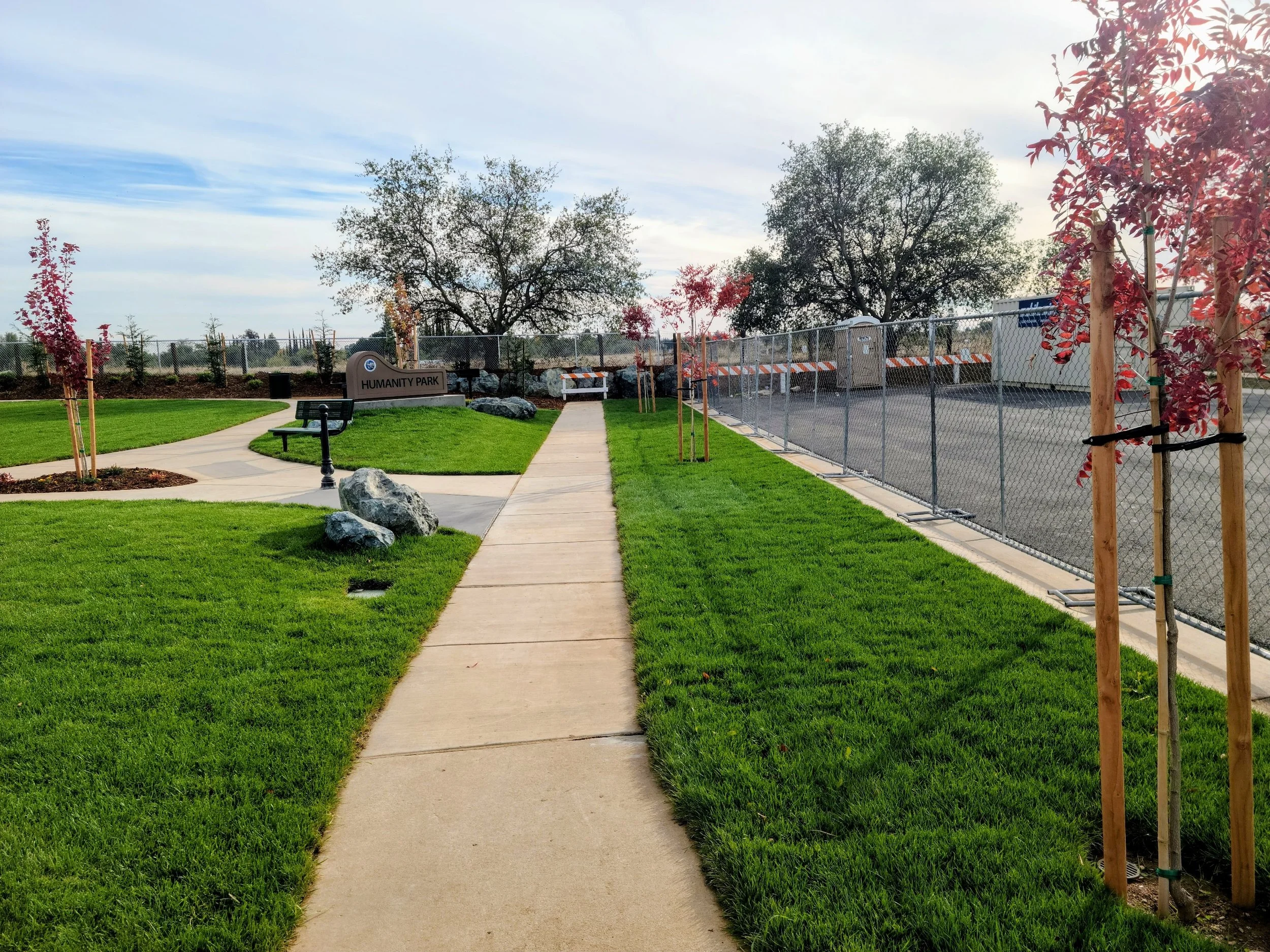Landscaping Yuba City community park with green lawns, walking paths, young trees, and gathering spaces.