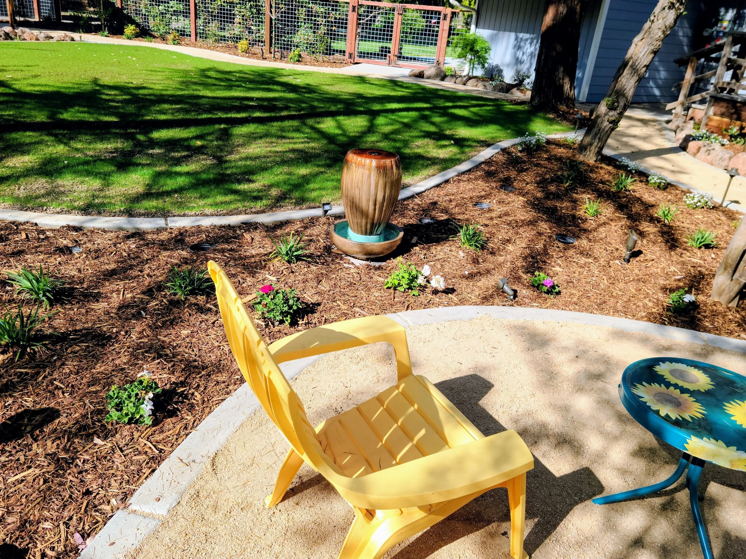 Landscaping Yuba City backyard with curved planting beds, fresh mulch, lawn, and relaxing patio seating area.