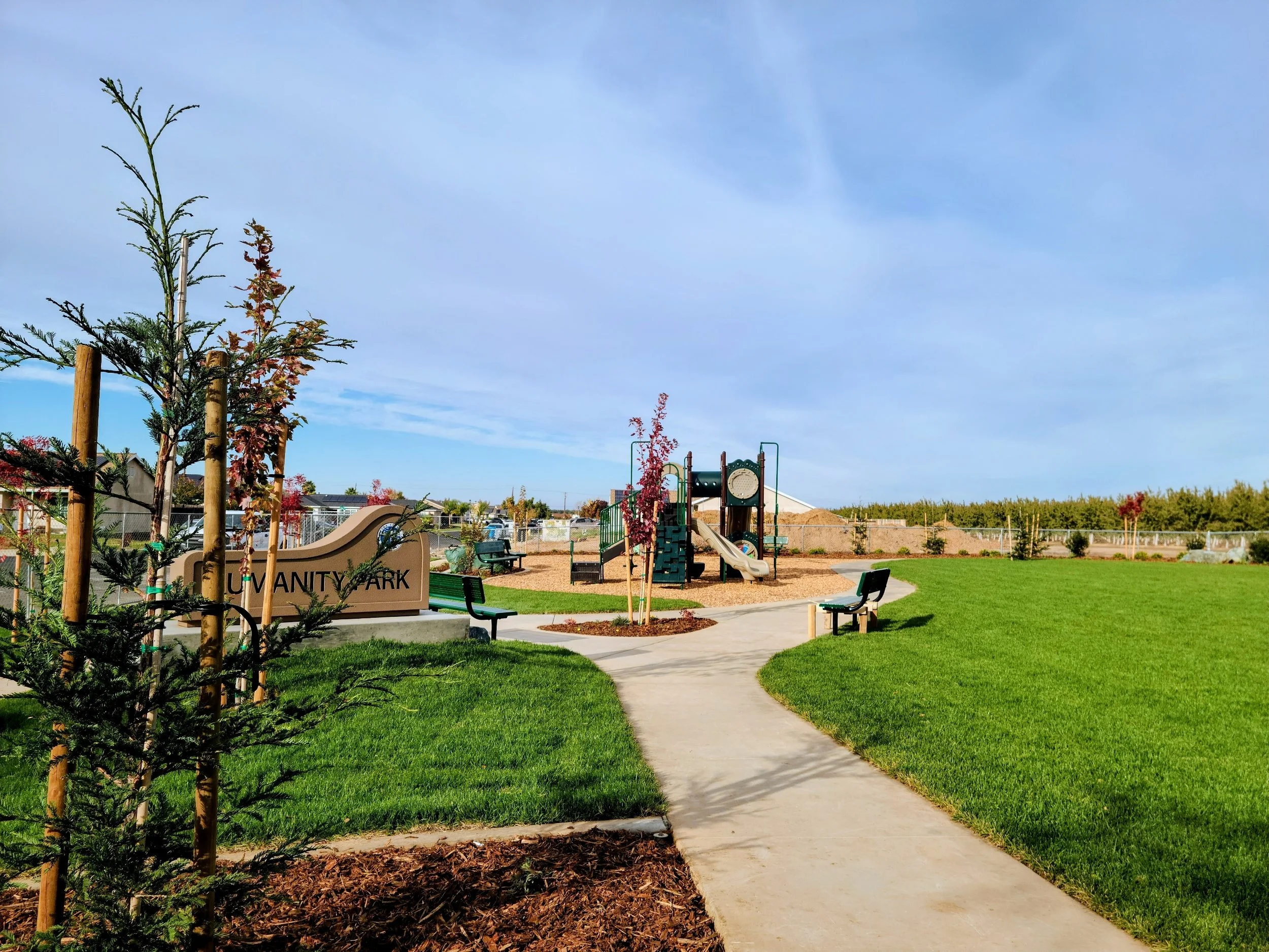 Community park with lush green lawn, walking paths, playground, and professionally installed landscape design.