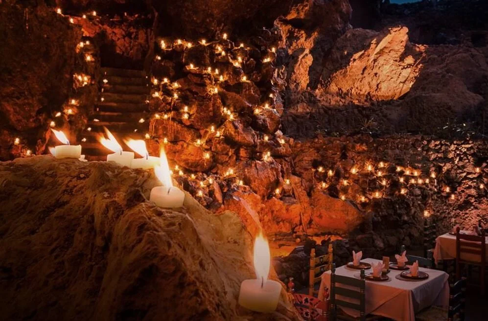 Dining area with candles and string lights on rocks, set for a meal with tables and chairs.