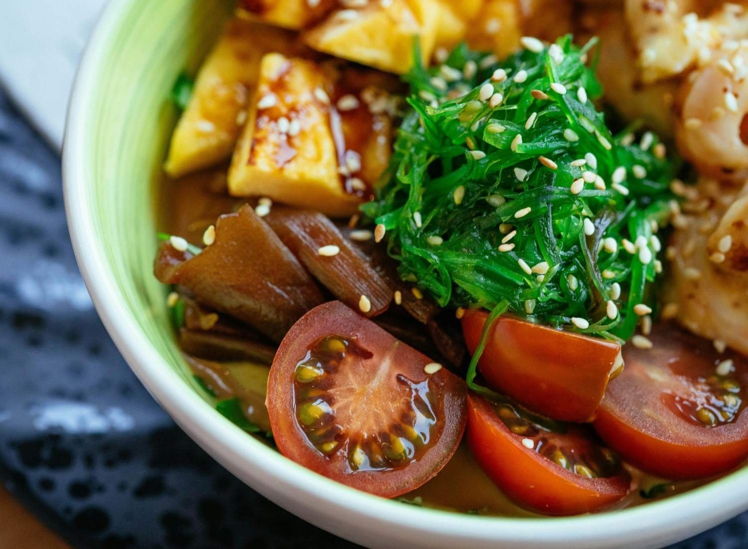 Close up of a prawn, tofu soup with seaweed and sesame seeds.