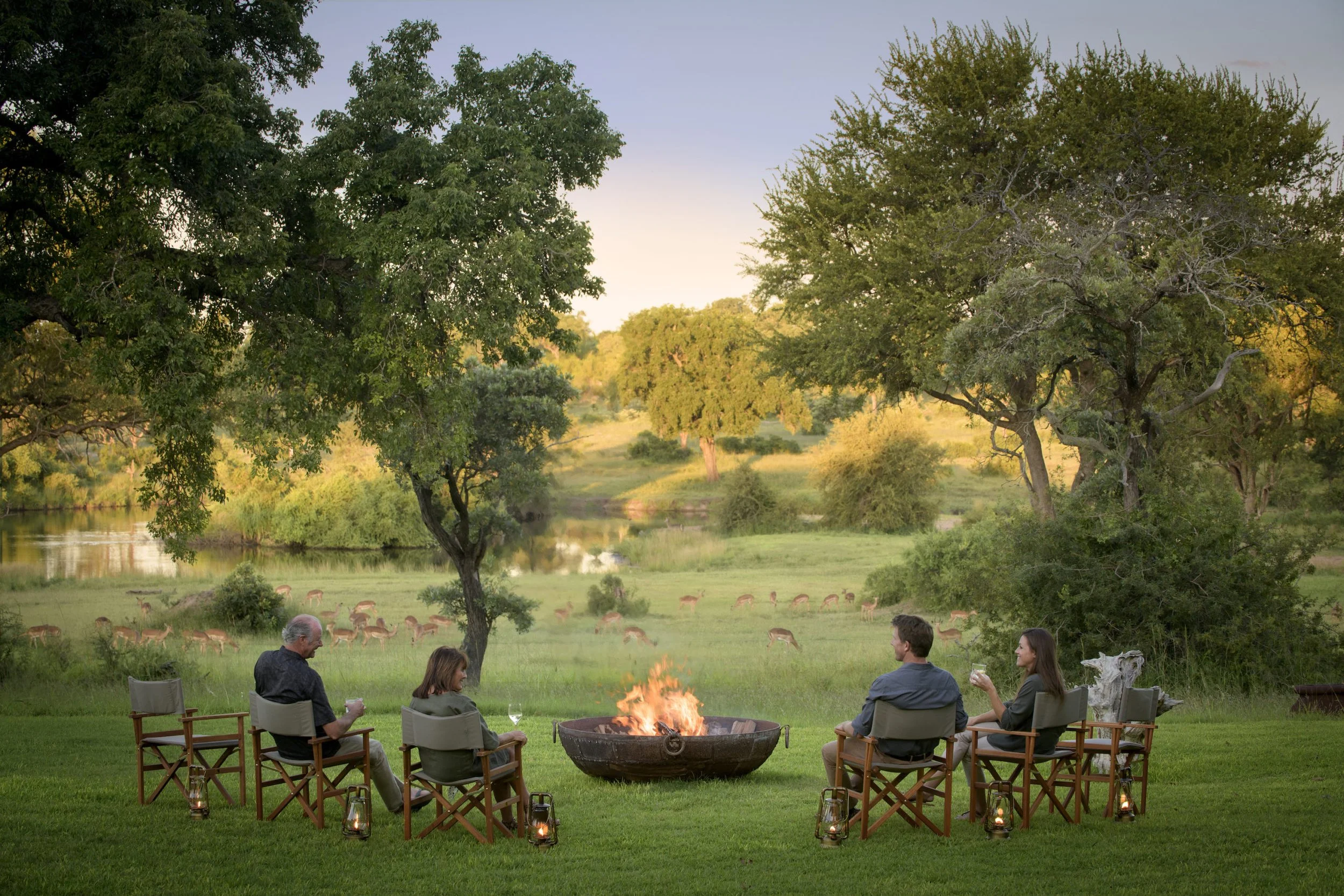 Guests enjoying drinks around a firepit at Singita Castleton, overlooking wildlife and a river in a private luxury African safari setting.