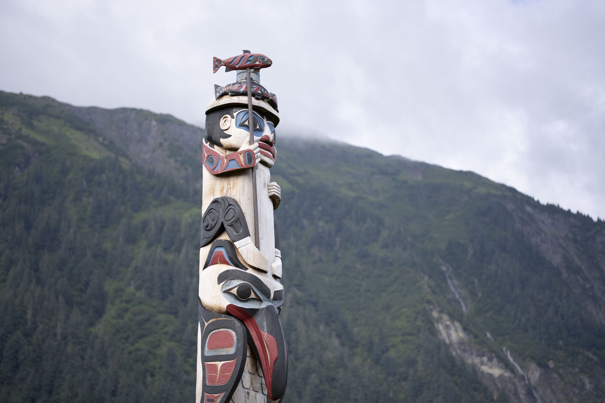 The top of a totem pole featuring a person holding a fish on a stick.
